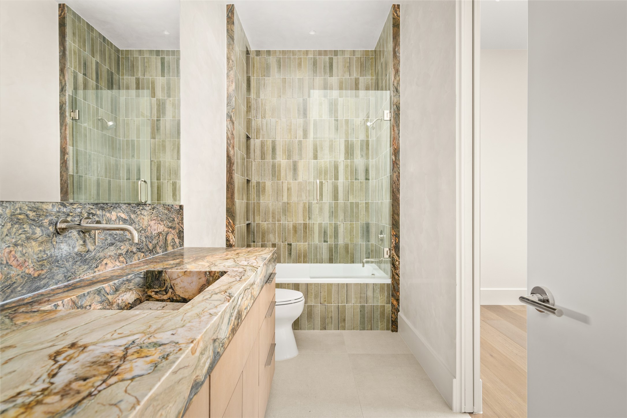 A stunning Fusion quartzite vanity with an integrated sink takes center stage in this elegant ensuite bath, complemented by a spacious glass-enclosed shower and beautifully coordinated stone finishes.
