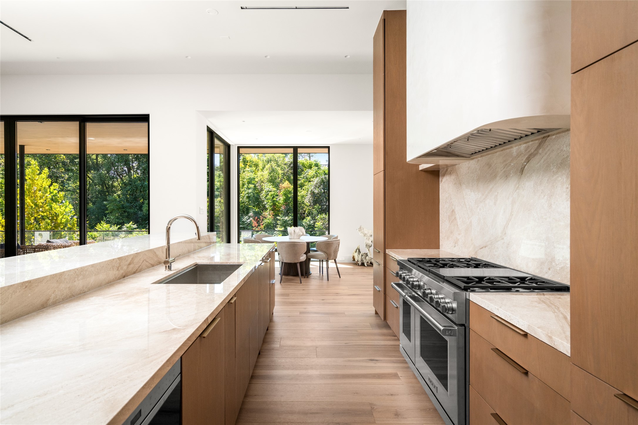 A closer look at the chef's kitchen highlights the 48-inch Wolf dual-fuel range, full-height Daino Reale marble backsplash, and generous island preparation space, with the sunlit breakfast room just beyond.