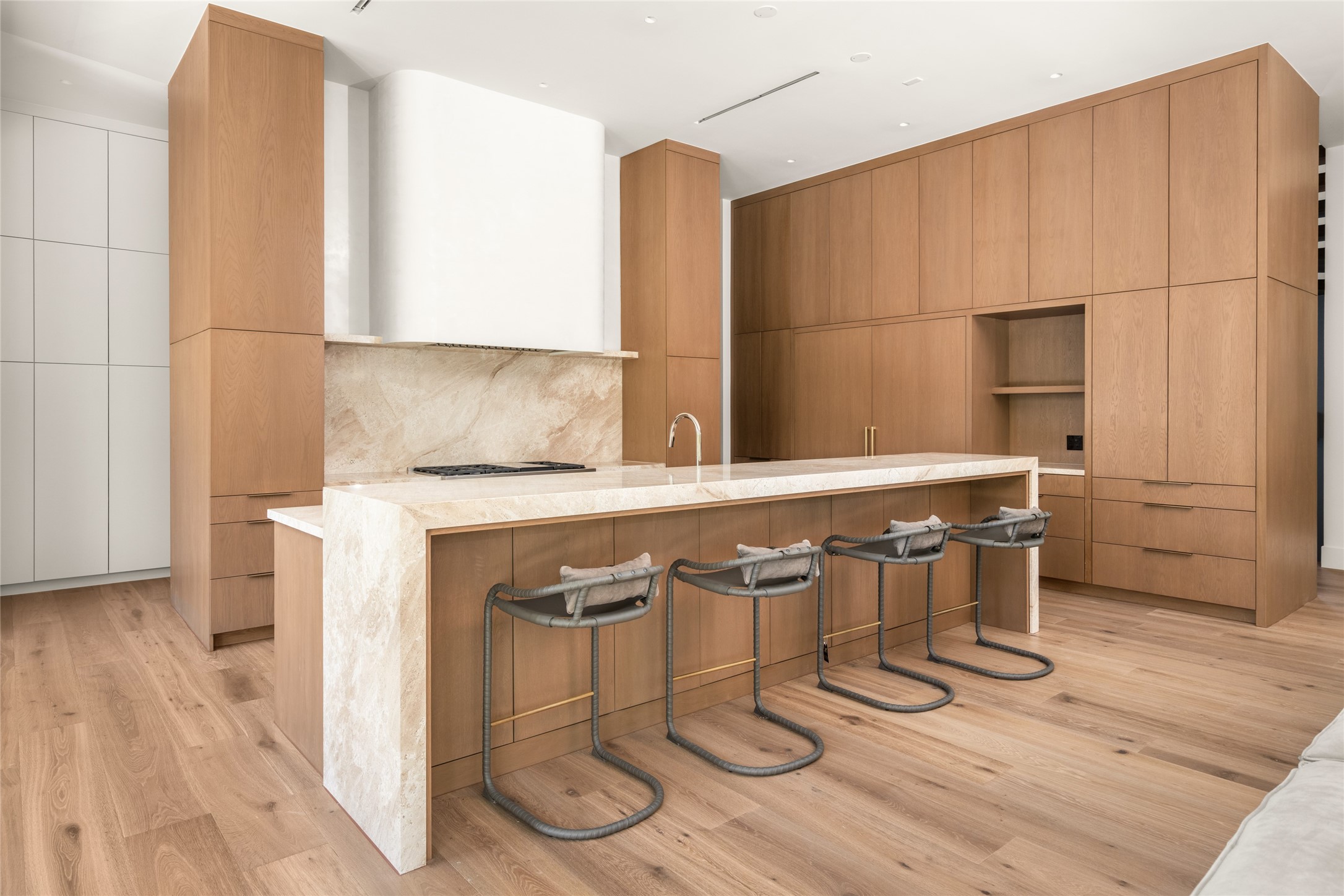 Floor-to-ceiling custom white oak cabinetry provides extensive storage while seamlessly concealing a 72-inch Sub-Zero refrigerator/freezer and dual panel-ready dishwashers, preserving the kitchen's clean architectural design.