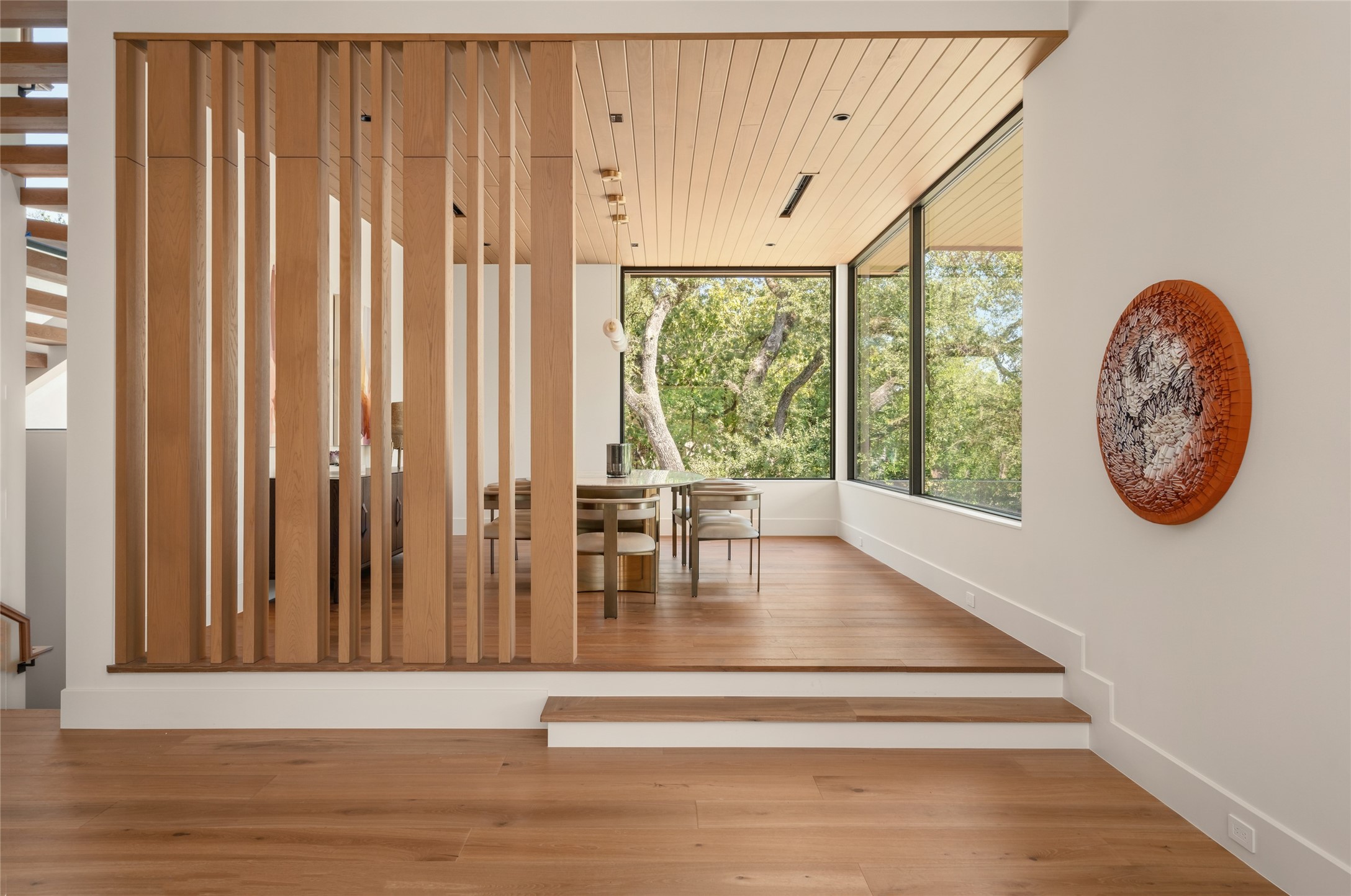 A subtle change in elevation gives the dining room its own identity, while custom white oak slatted partitions define the space without closing it off. Expansive windows bring in natural light and frame the surrounding trees.