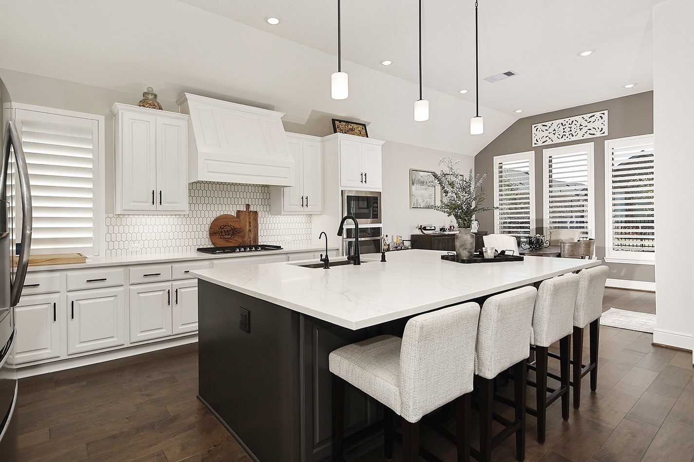 Custom white cabinetry features modern black pulls that coordinate perfectly with the black kitchen faucet and pendant lighting. The honeycomb-patterned white tile backsplash adds unique character and visual interest to the space.