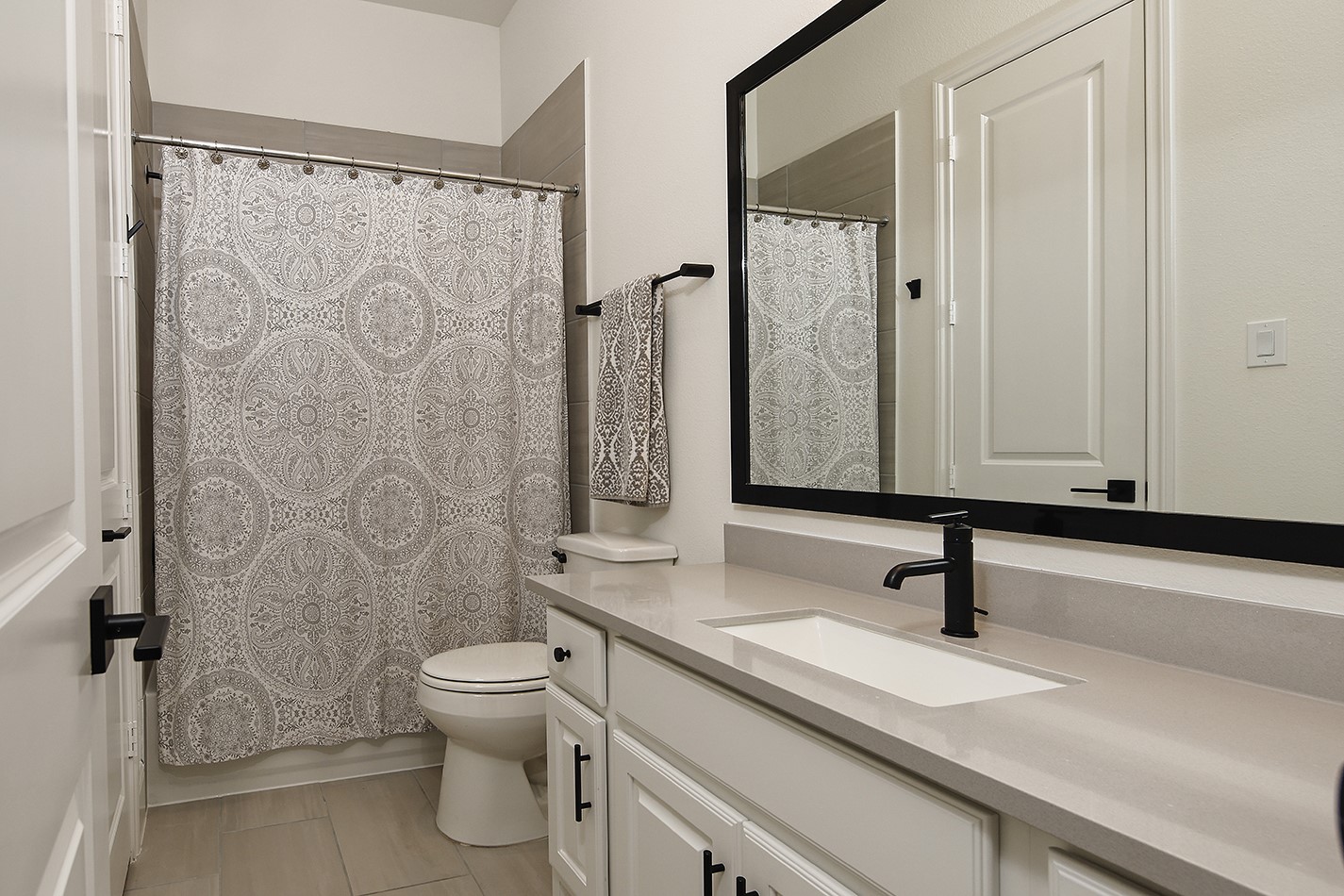 The full bathroom features premium quartz countertops complemented by a modern rectangular sink, matte black fixtures, matching cabinet hardware, and a contemporary framed mirror.