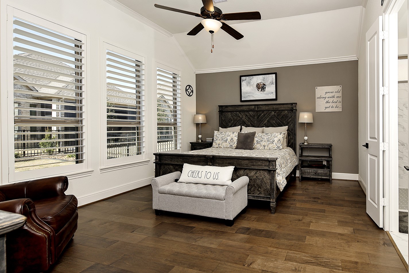 Spacious primary suite featuring a wall of windows adorned with plantation shutters, elegant crown molding, and rich hardwood flooring for an upscale aesthetic.