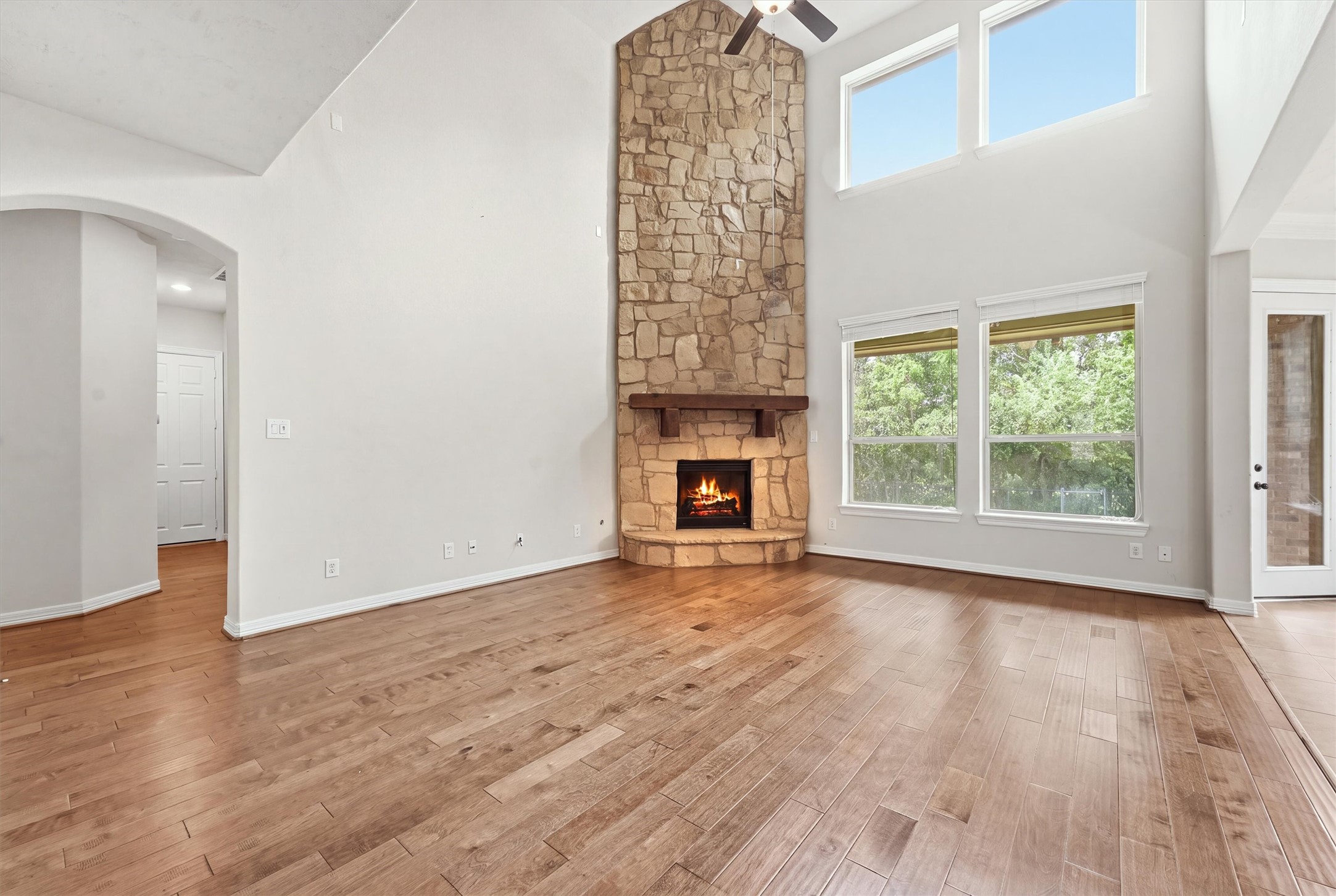 Another view of the living room, featuring large windows,floor to ceiling stacked stone fireplace and beautiful wood floors