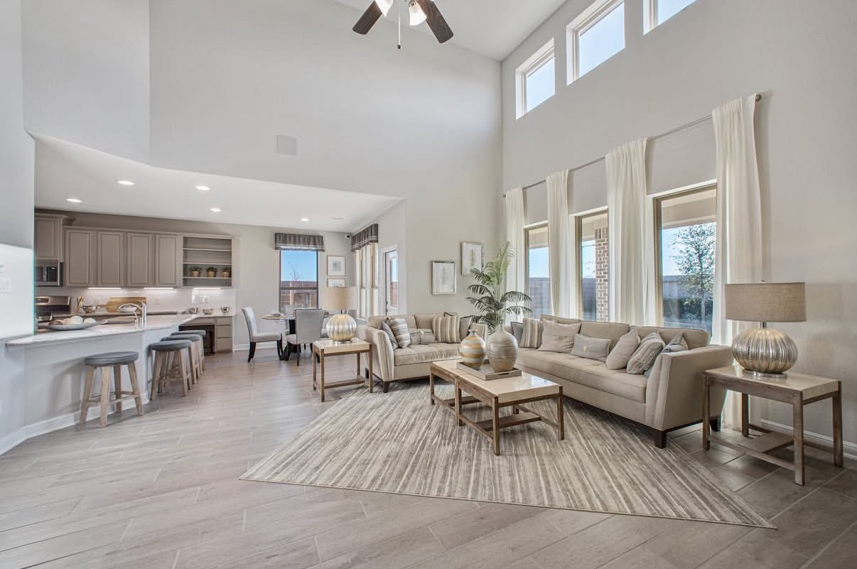 Spacious living area with vaulted ceilings, abundant natural light, and an open floor plan seamlessly connecting to a modern kitchen with a breakfast bar.