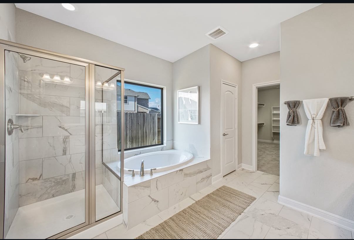Elegant bathroom featuring a spacious glass-enclosed shower and a luxurious soaking tub with natural light pouring in through a large window.