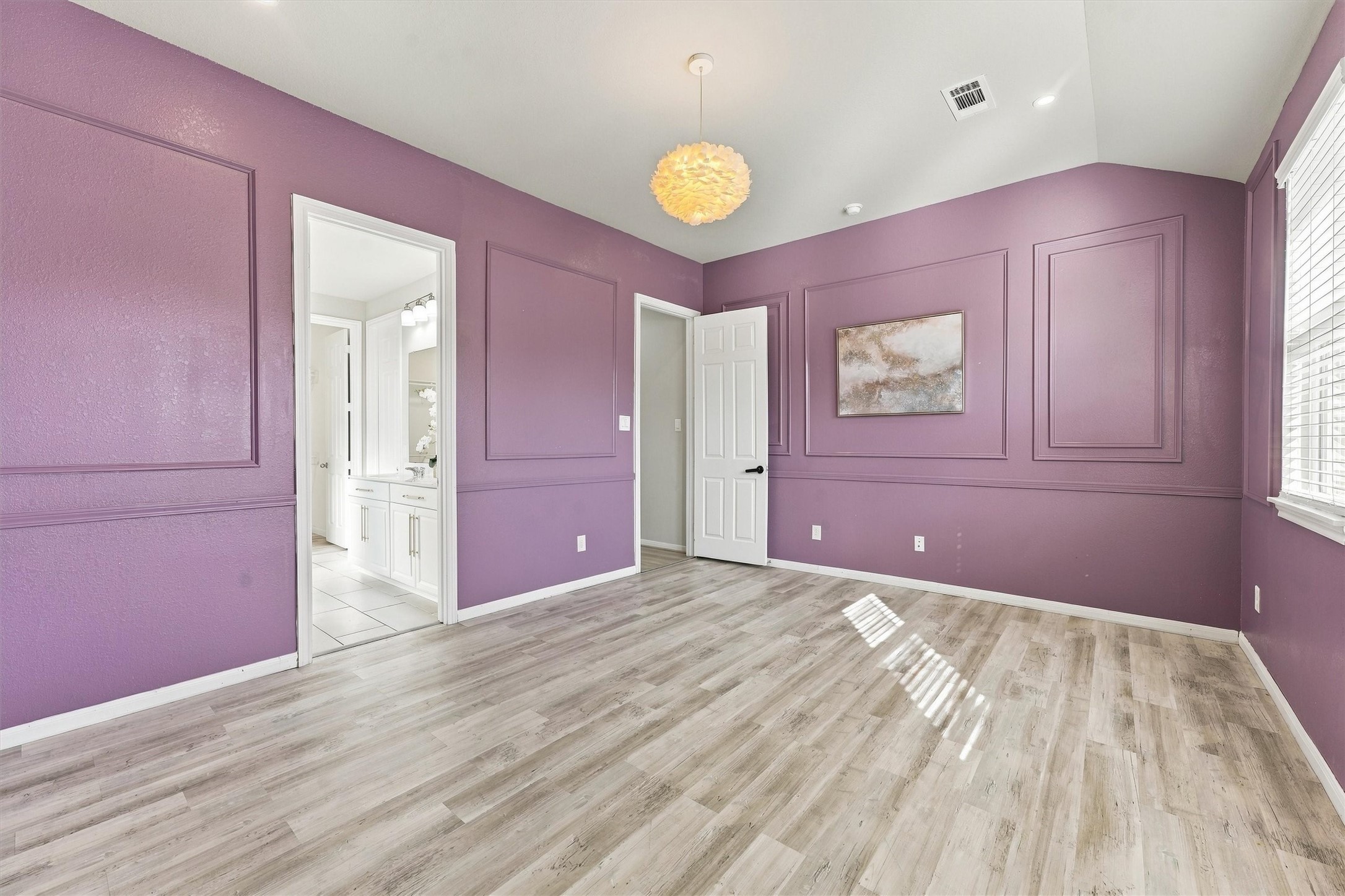 Distinctive primary bedroom with lavender walls, molding, three windows, and light wood-look flooring.