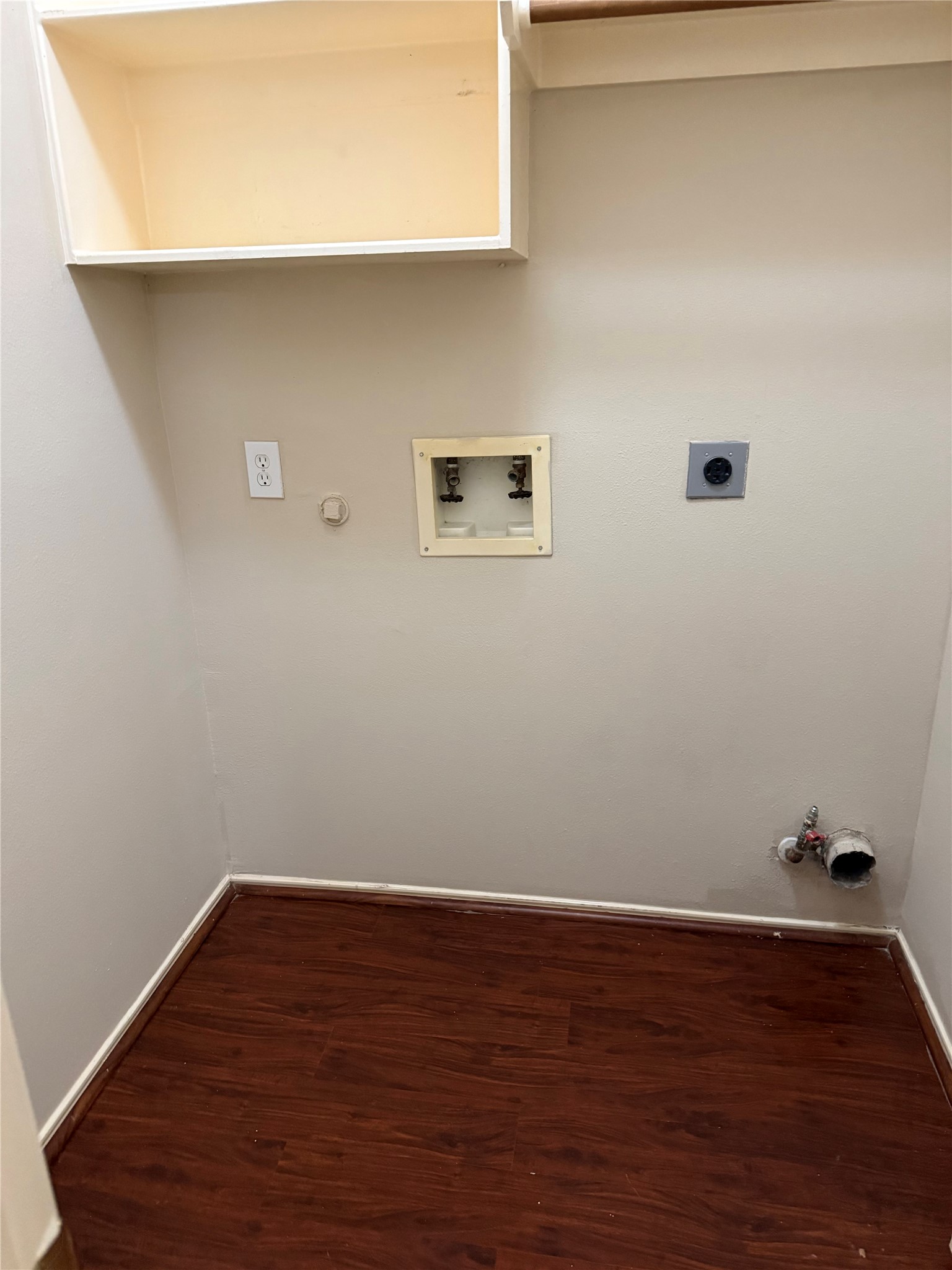 Spacious laundry room with hookups, featuring a convenient wall shelf and durable wood flooring.