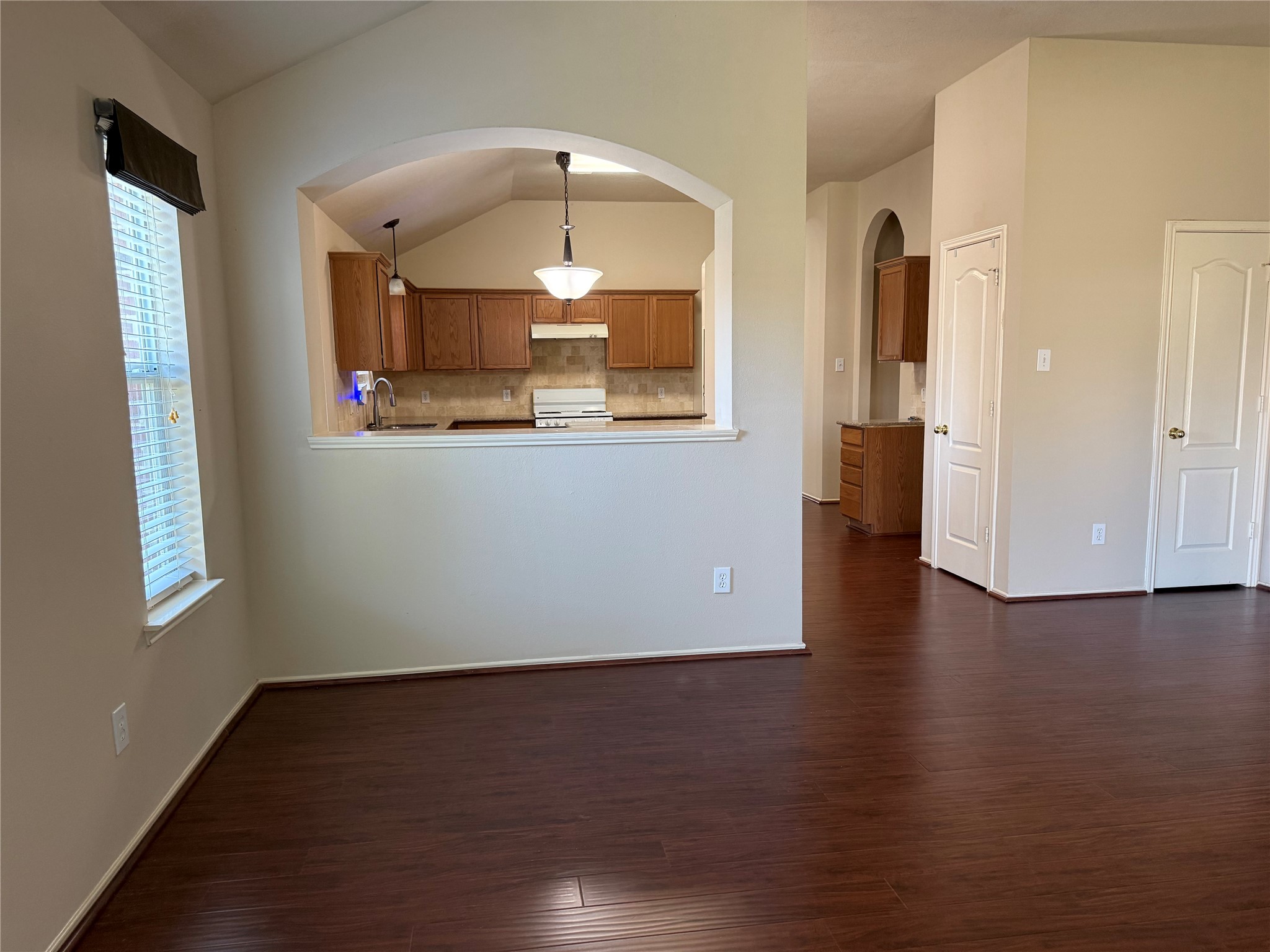 Bright and inviting open-concept living area with rich wood flooring, featuring a cozy kitchen with warm wooden cabinetry and a convenient pass-through opening.