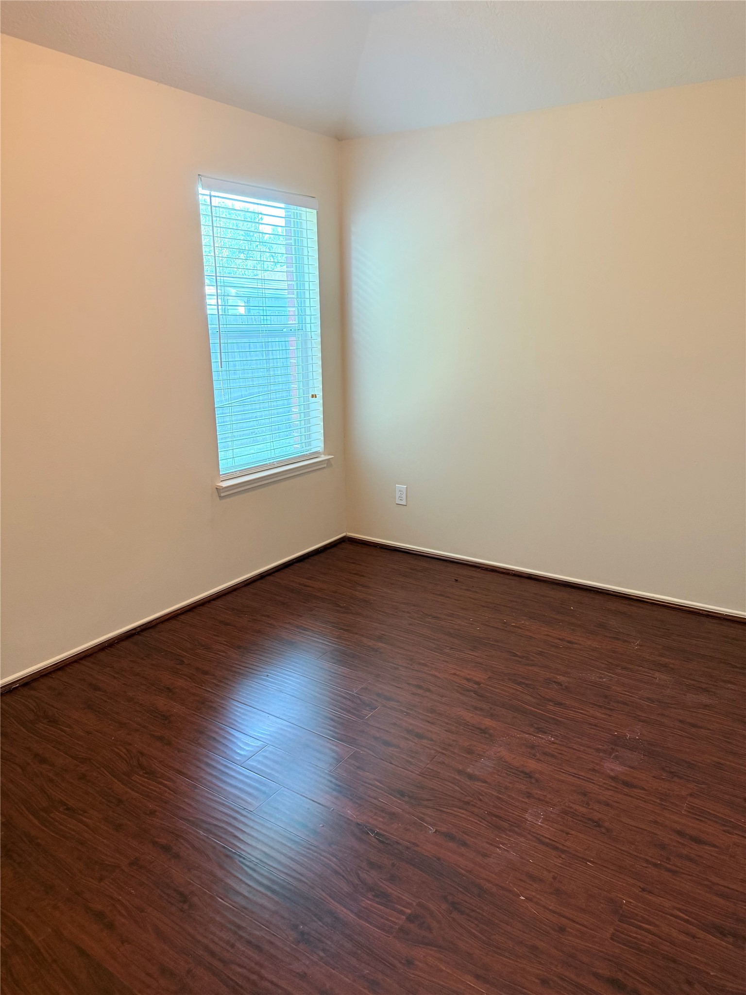 Cozy room with rich wood flooring and a large window providing natural light, perfect for a bedroom or home office.