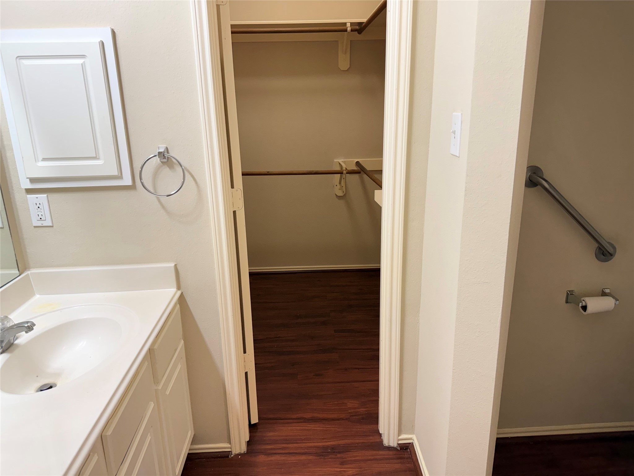 Spacious bathroom with a clean, white vanity leading to a large walk-in closet featuring rich wooden flooring.