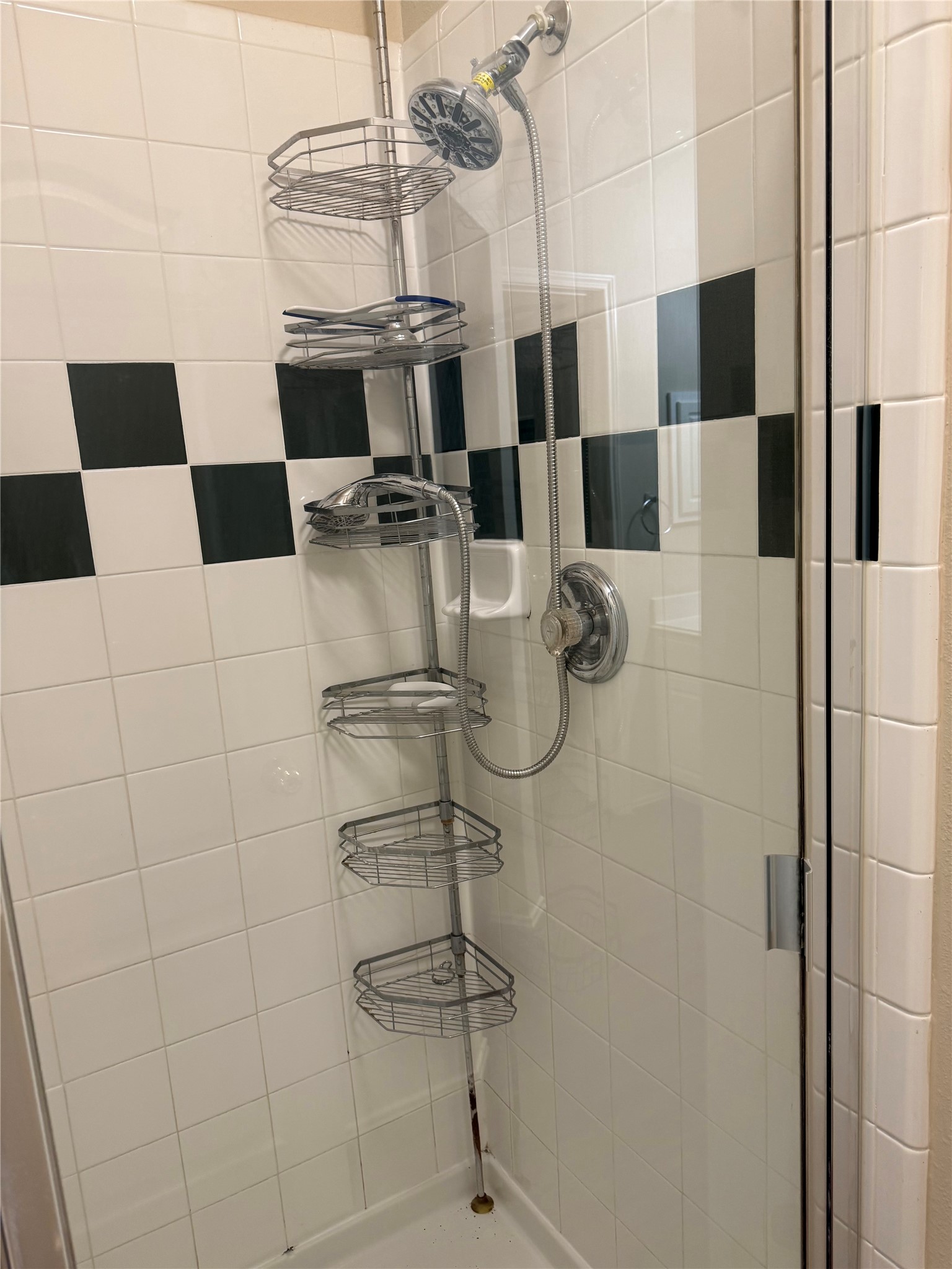 Modern shower with sleek chrome fixtures, glass door, and convenient storage shelves, set against a classic black and white tiled backdrop.
