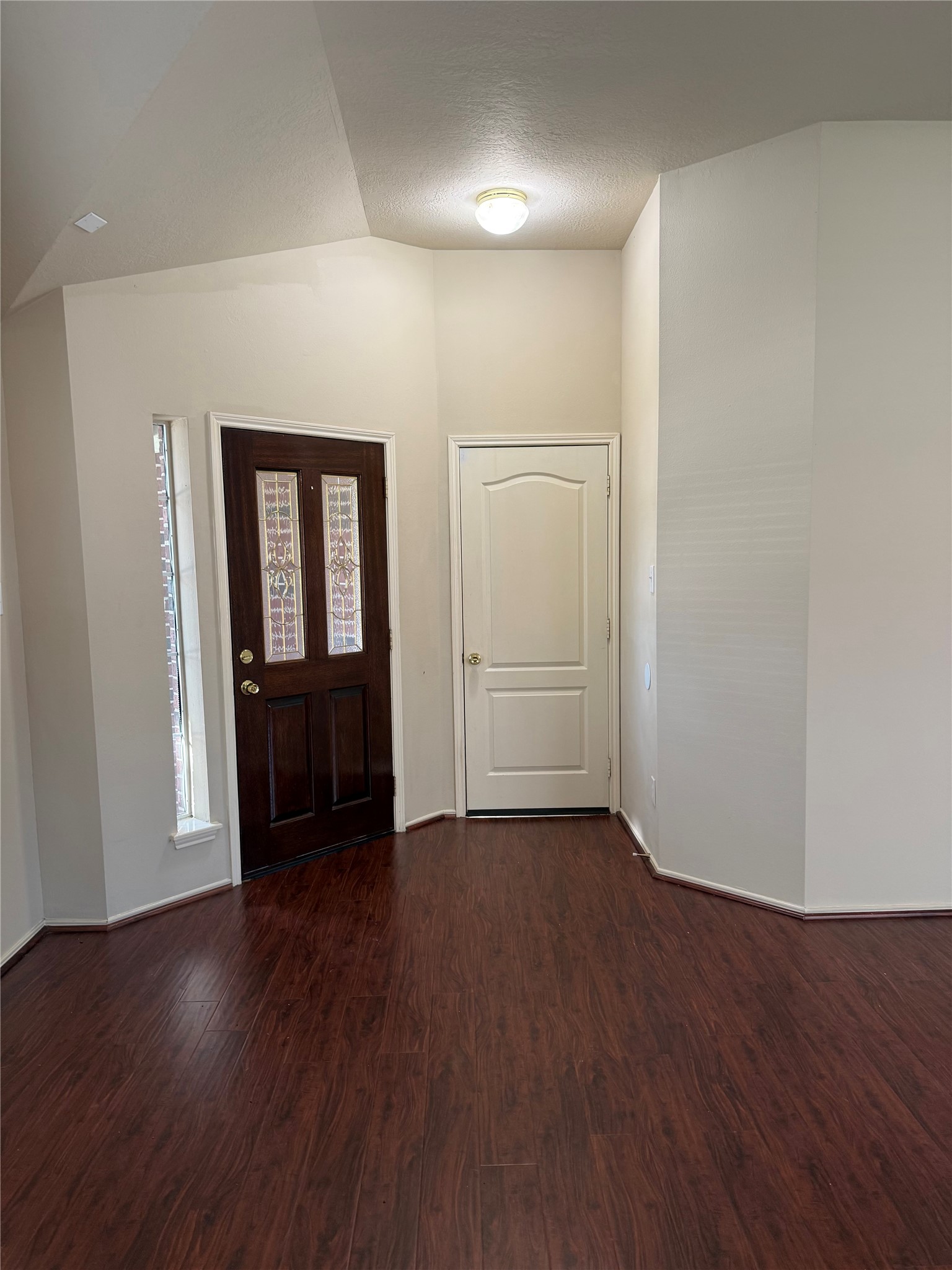 Inviting entryway with rich wood flooring, a stylish front door with glass accents, and a convenient closet for storage.