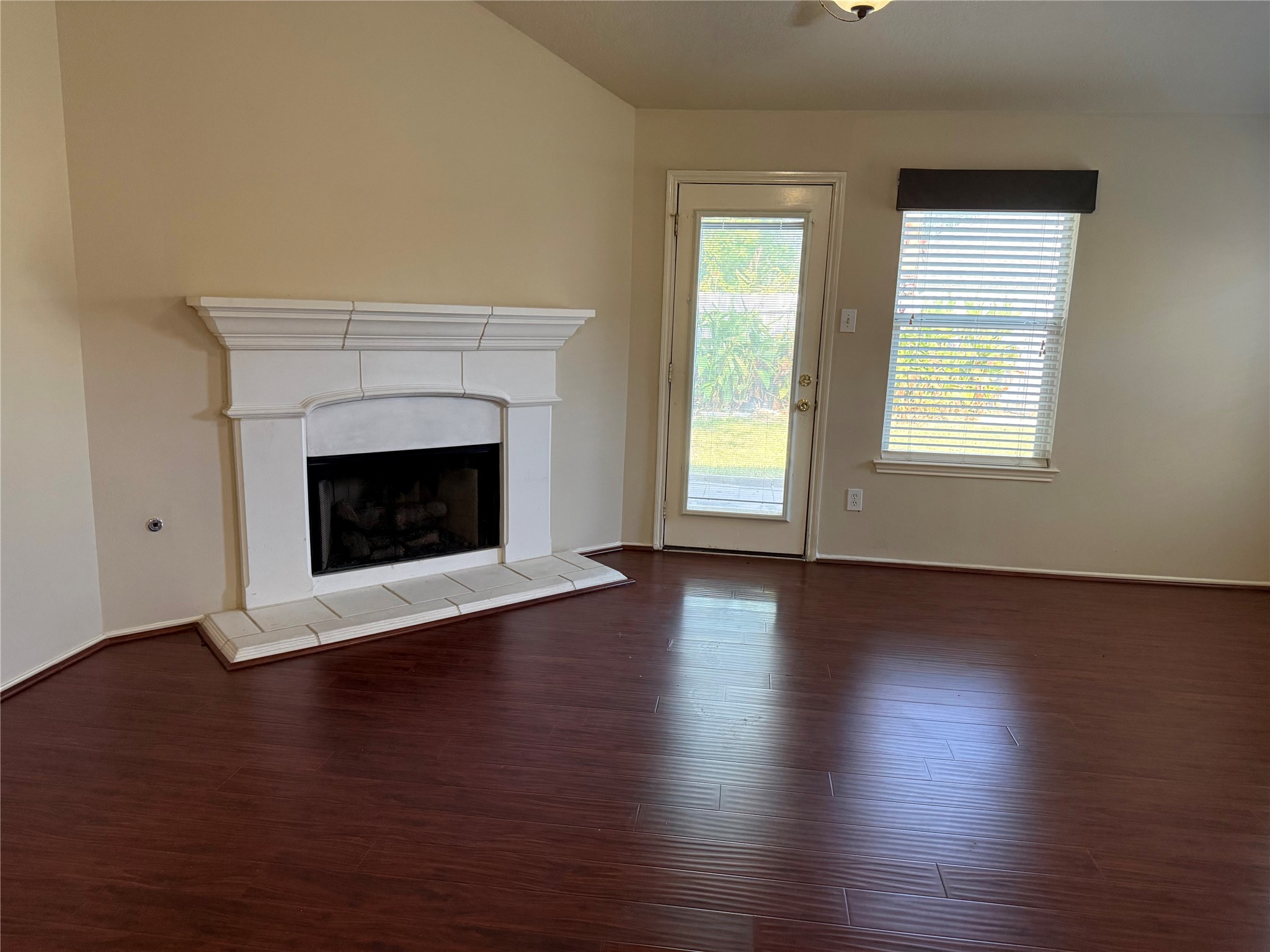 Inviting living area featuring a cozy fireplace, rich wood flooring, and abundant natural light from a large window and glass door leading outside.