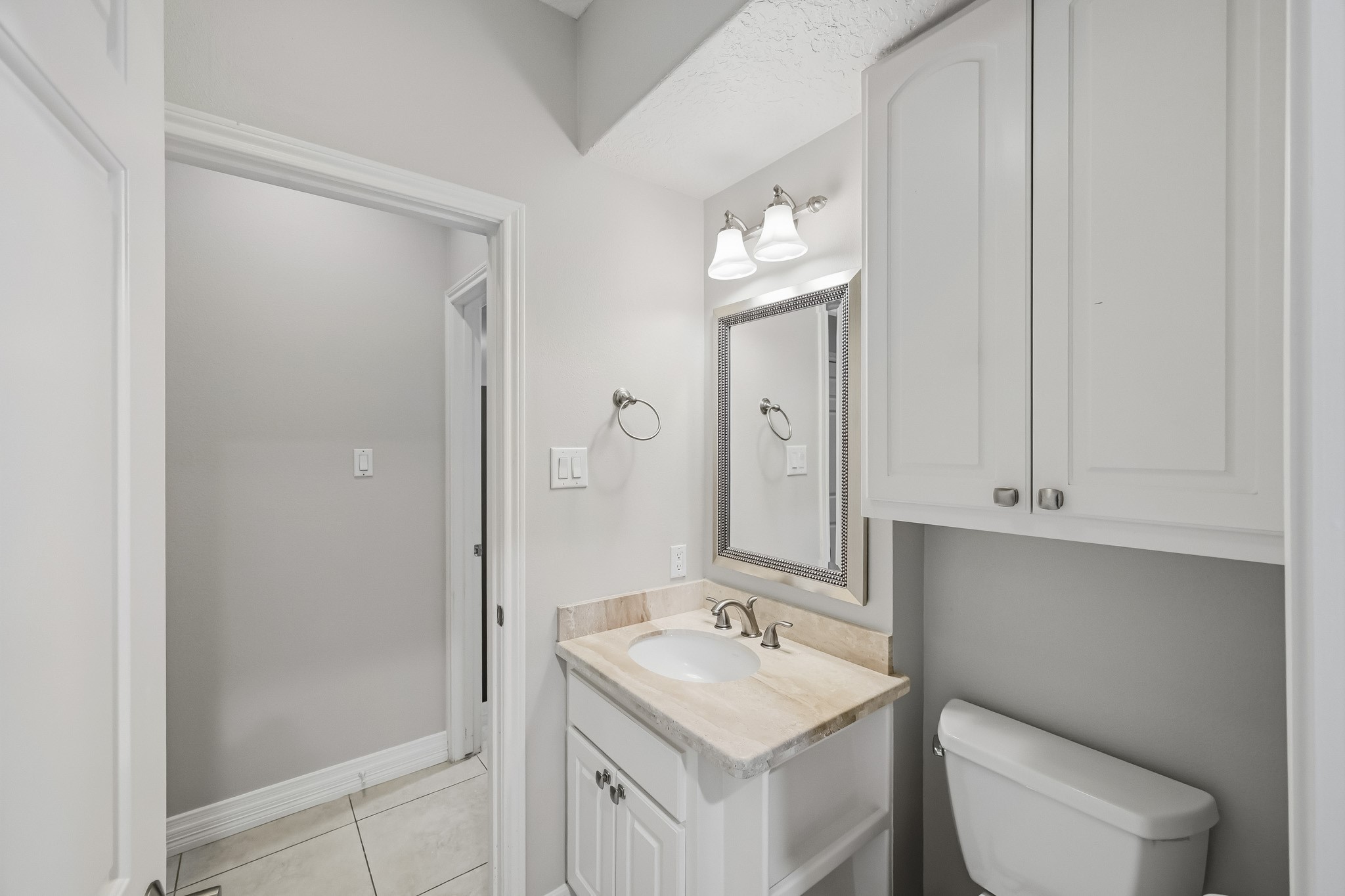 A convenient full bathroom adjoining the study features a stone-topped vanity, framed mirror, decorative lighting and built-in storage.