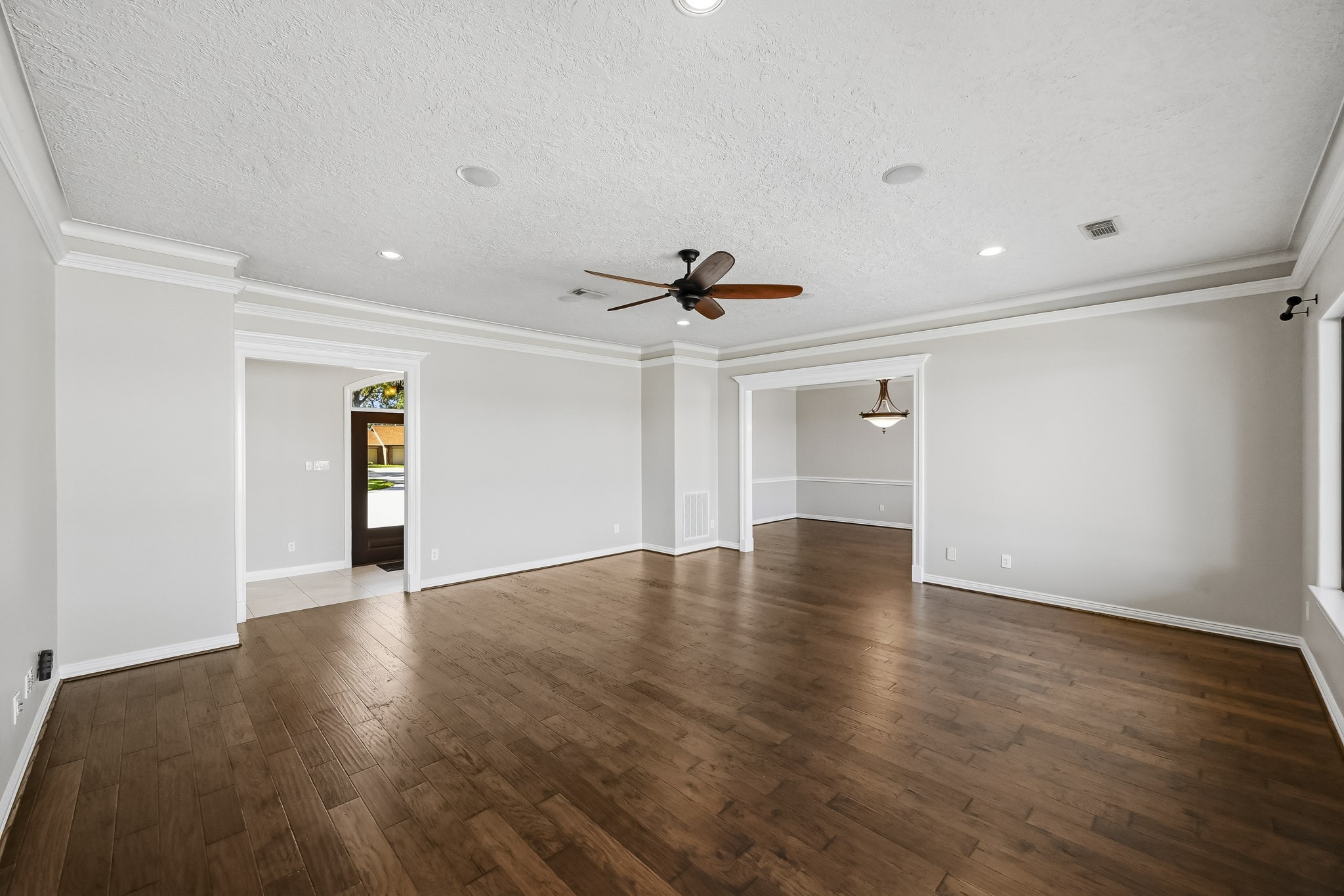 The expansive living room showcases wood-look tile flooring, crown molding, a tray ceiling, recessed lighting and a ceiling fan.