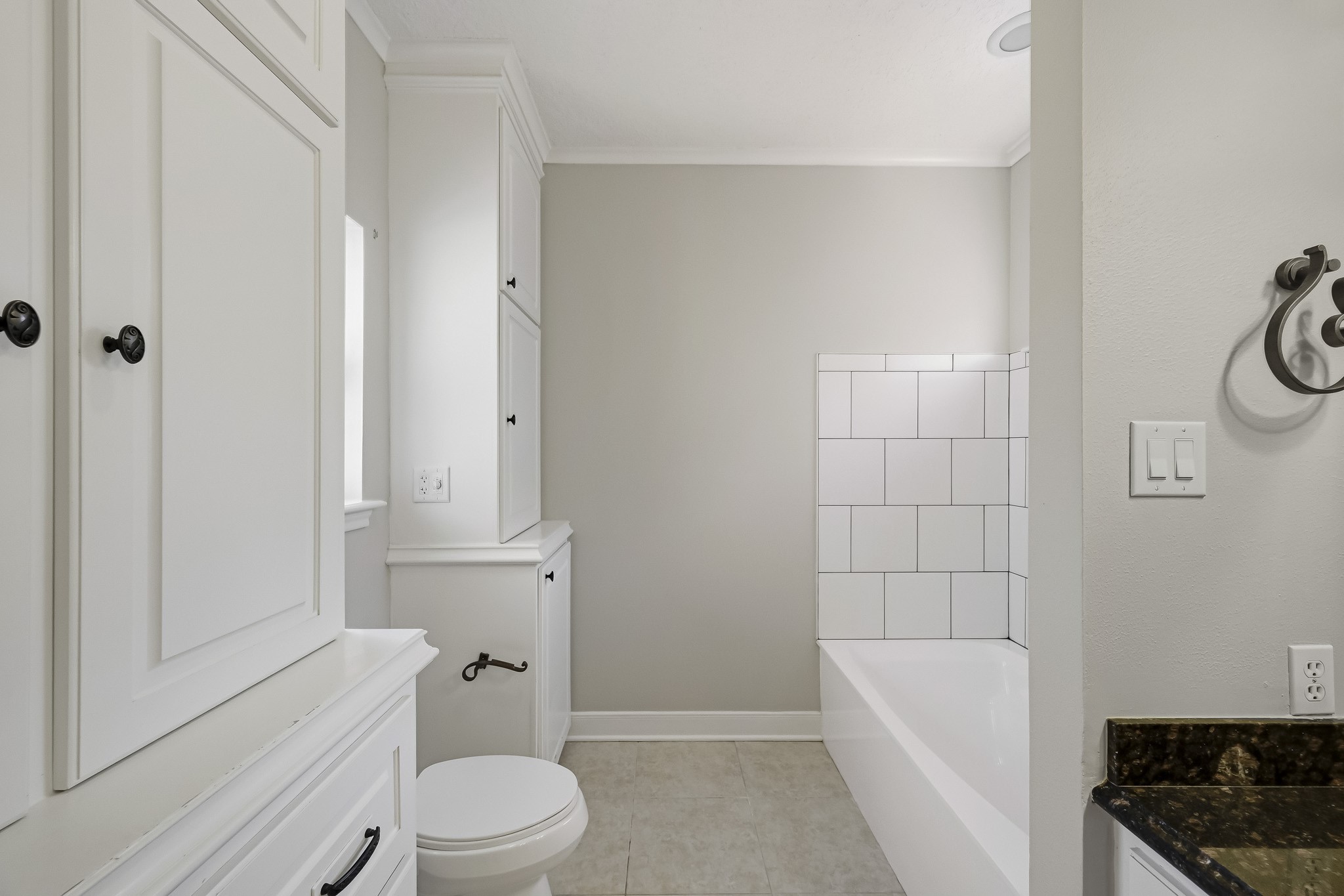 Unwind in the soaking tub featuring an updated tile surround, neutral finishes and convenient built-in storage cabinetry.
