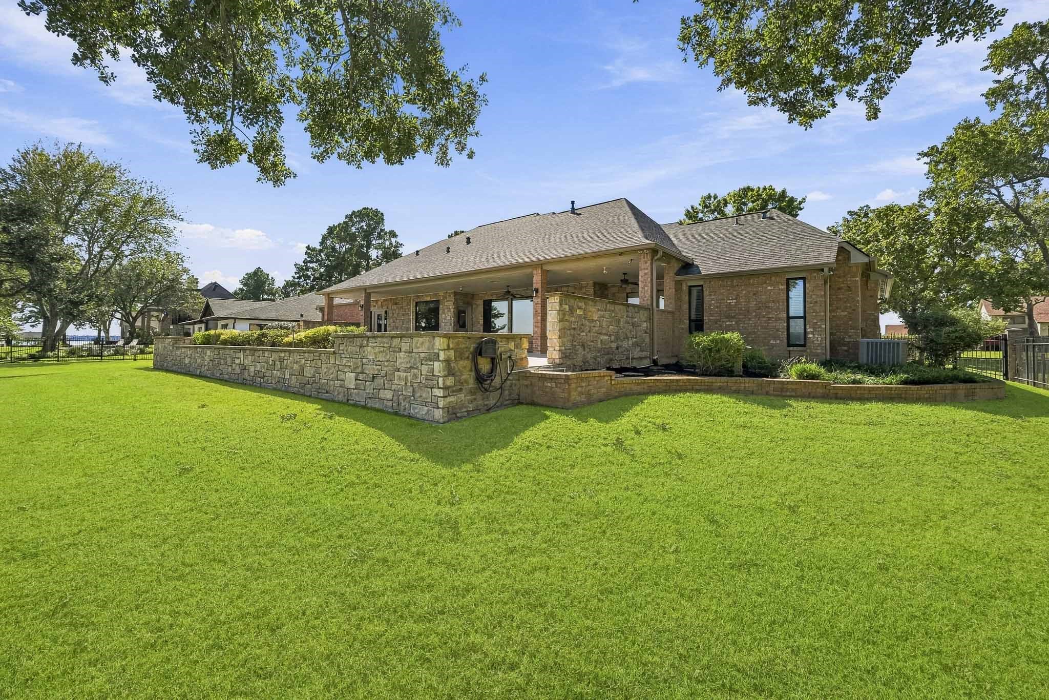 Mature shade trees, a lush green lawn and an impressive terraced stone wall create a picturesque setting around the elevated pool and patio.