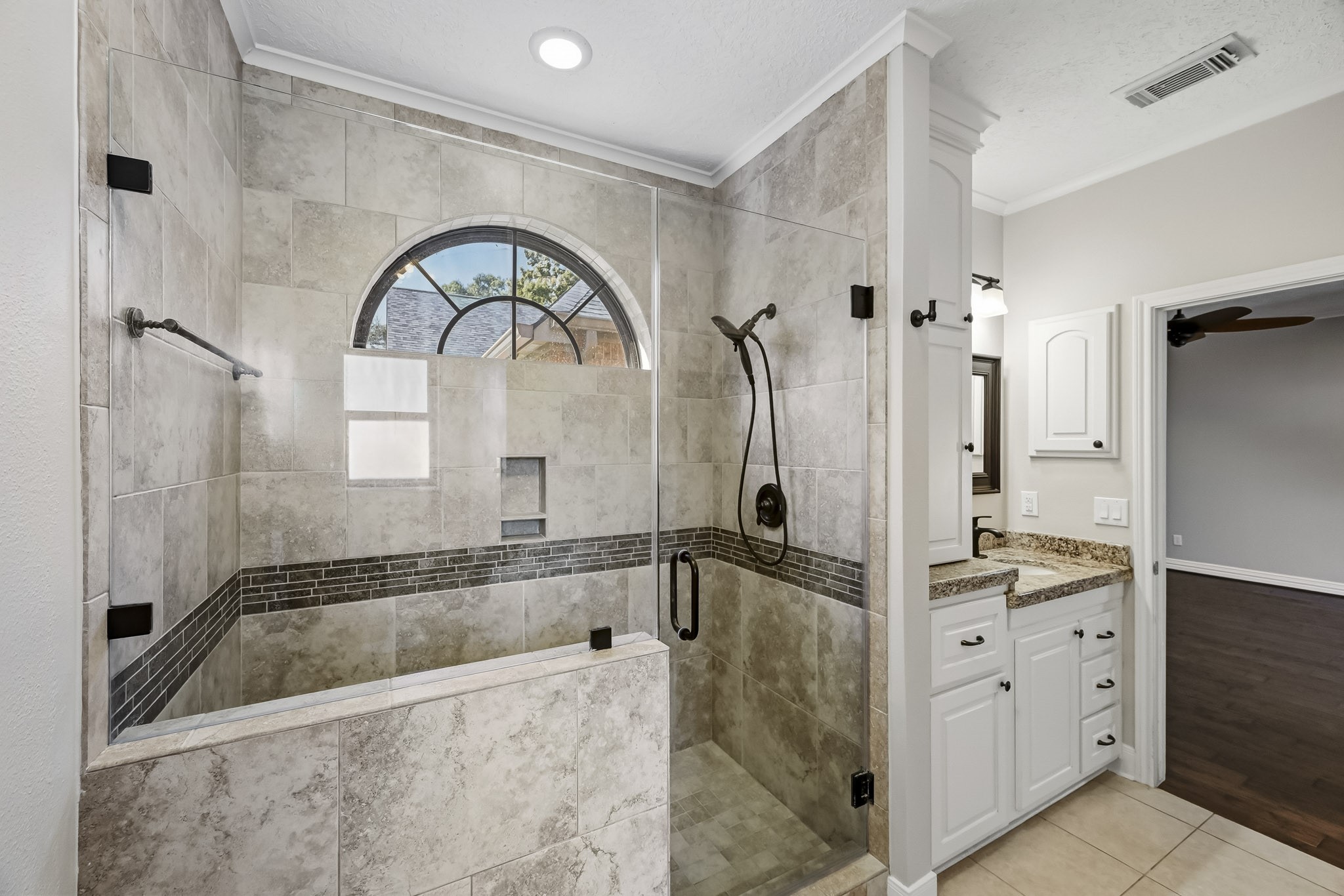 This impressive walk-in shower features floor-to-ceiling tile, a frameless glass enclosure, decorative accents, built-in niches and an elegant arched window!