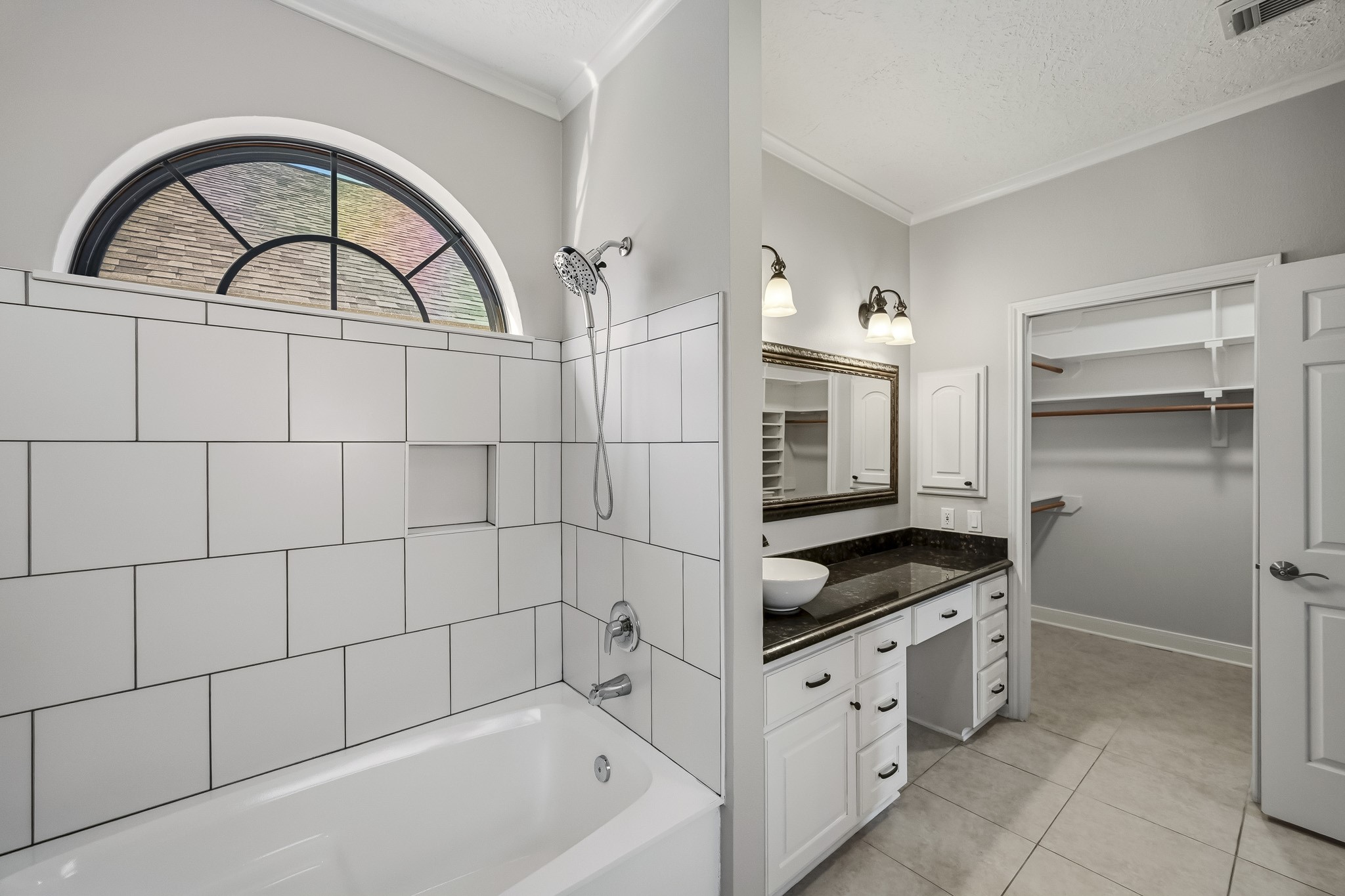 A beautiful arched window adds architectural charm above the soaking tub, while an adjoining walk-in closet provides convenient storage.