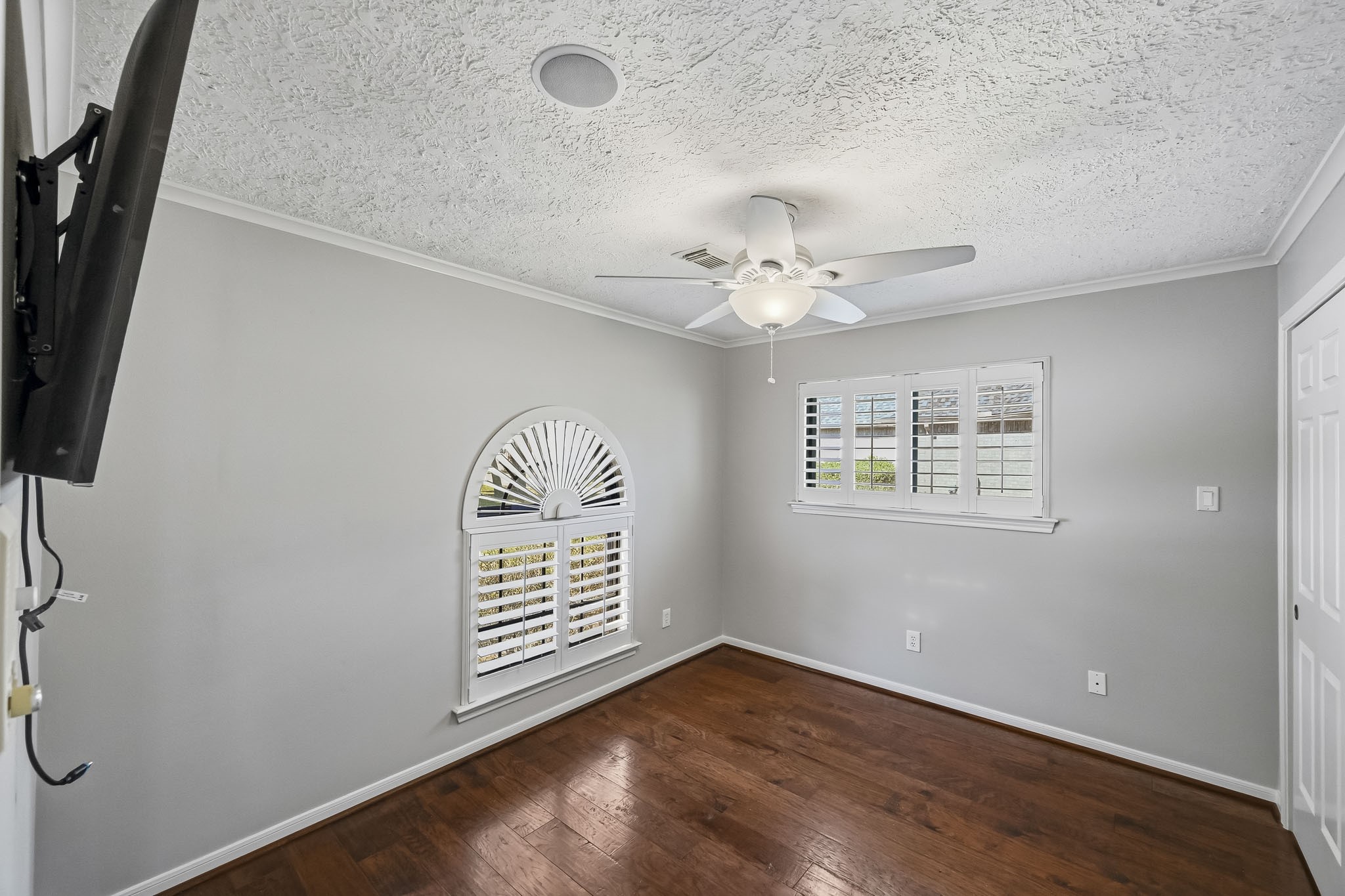 Bedroom #3 features wood-look tile flooring, crown molding, a ceiling fan and a charming arched window with plantation shutters.