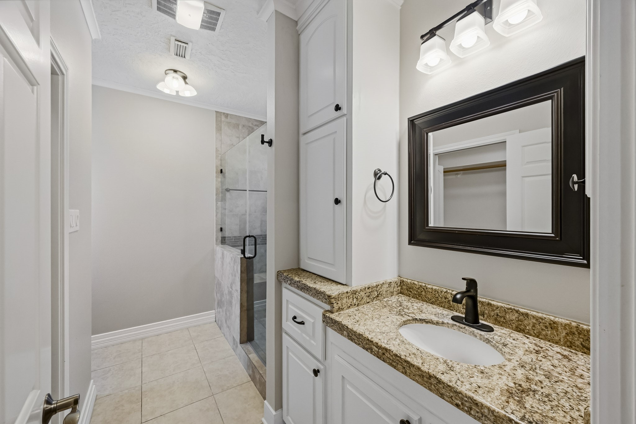 The second primary bathroom features a granite-topped vanity, updated fixtures, generous cabinetry and a beautifully tiled walk-in shower.