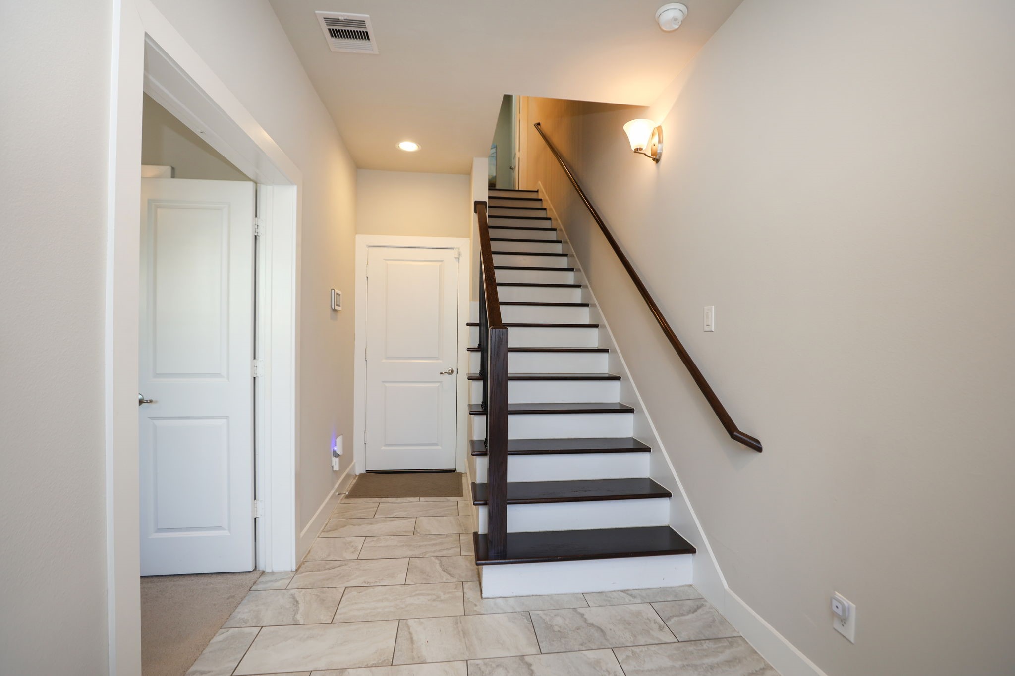View as you enter the home, featuring marble style tile and hardwood floors going up the stairs. Double doors to your left enter the first bedroom/office. Door in center goes to your garage.