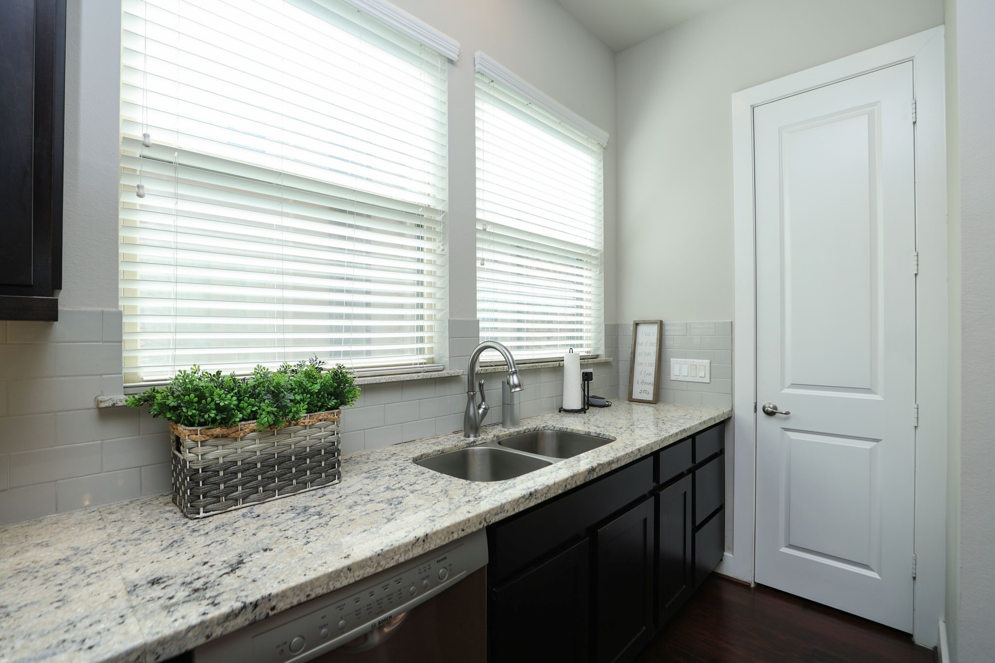 View of the sink with 2 large windows, window coverings, and door to your full pantry. Home appears basically new with modern touches and paint.