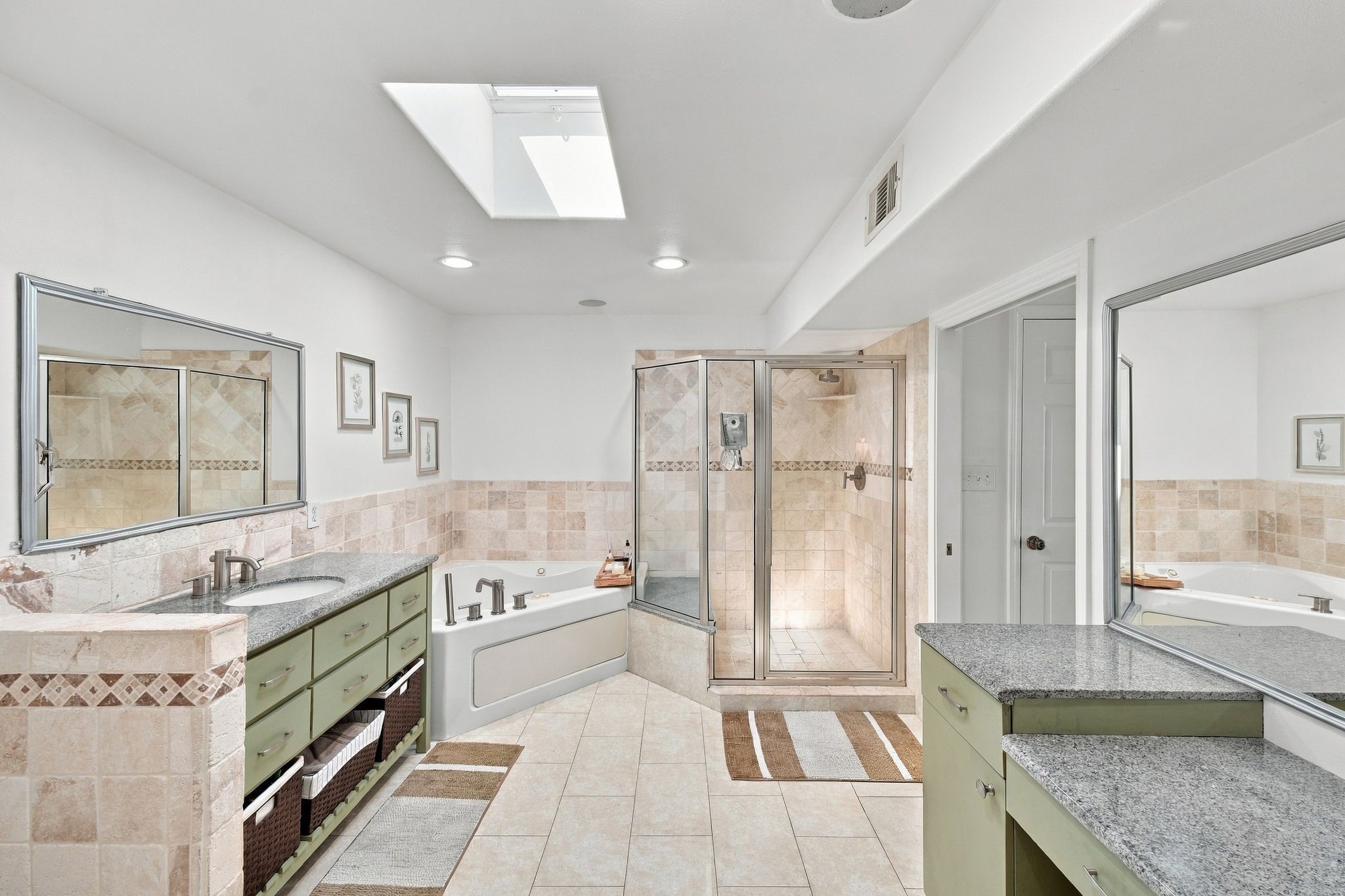 Spacious bathroom featuring a luxurious soaking tub, glass-enclosed shower, dual sinks with granite countertops, and vanity.