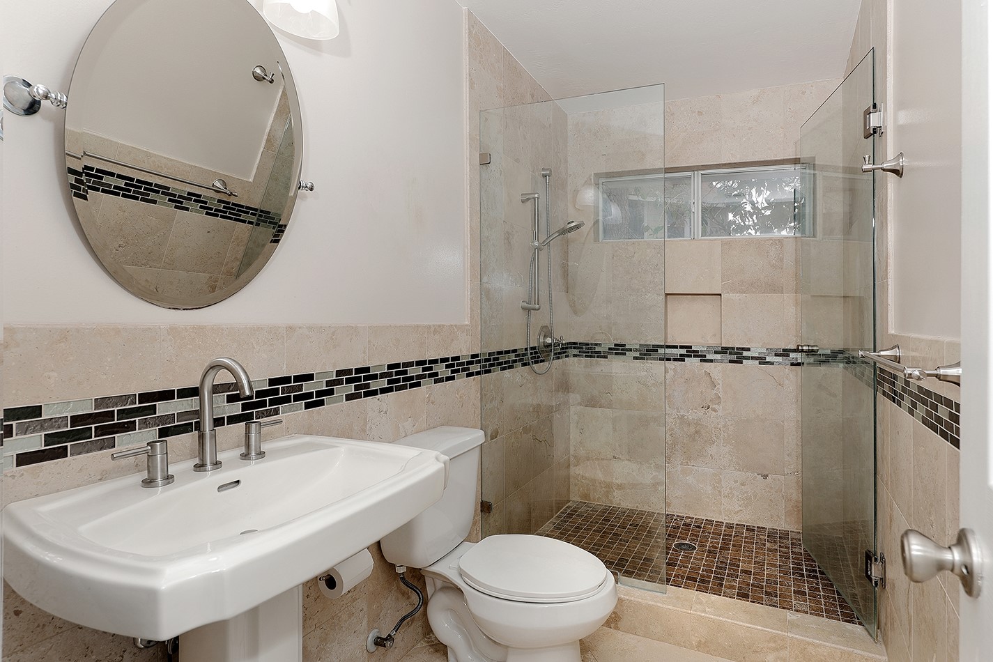 Modern bathroom featuring a glass-enclosed shower with stylish tile accents, a sleek pedestal sink, and a round mirror.