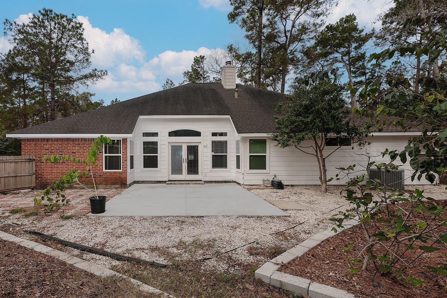 The back yard features a spacious concrete patio, surrounded by a low-maintenance landscape with trees and a wooden fence, providing a private and serene outdoor space.