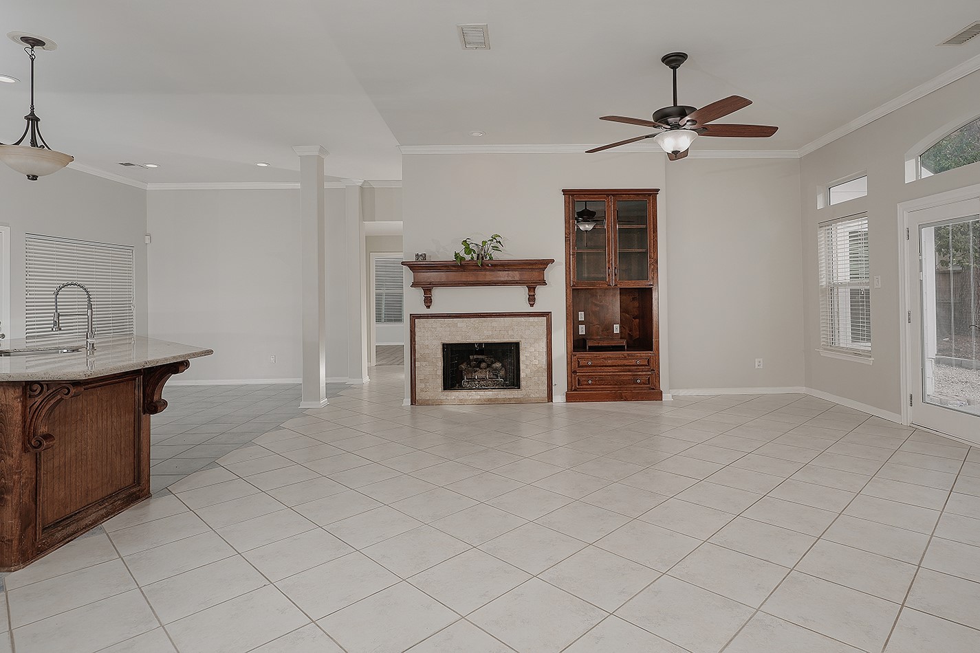 Bright and spacious open-concept living area with tile flooring, a central fireplace with a wooden mantel and built-in shelving.