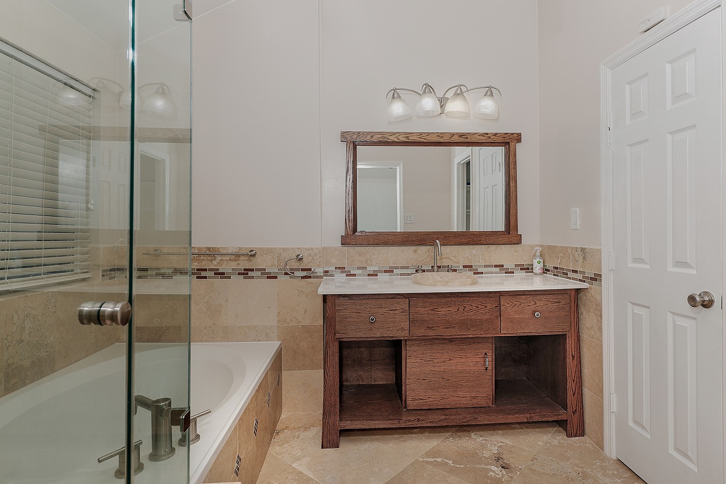 This bathroom features a modern design with a glass-enclosed bathtub, a wooden vanity with a large mirror, and elegant tile accents.