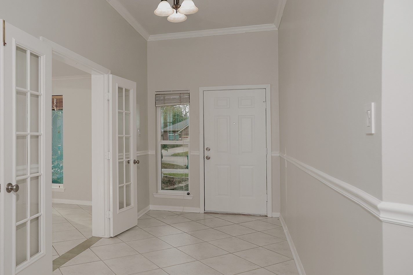 A welcoming entryway with neutral tones, featuring a tiled floor, crown molding, and French doors leading to the study. A welcoming entryway with neutral tones, featuring a tiled floor, crown molding, and French doors leading to the study.
