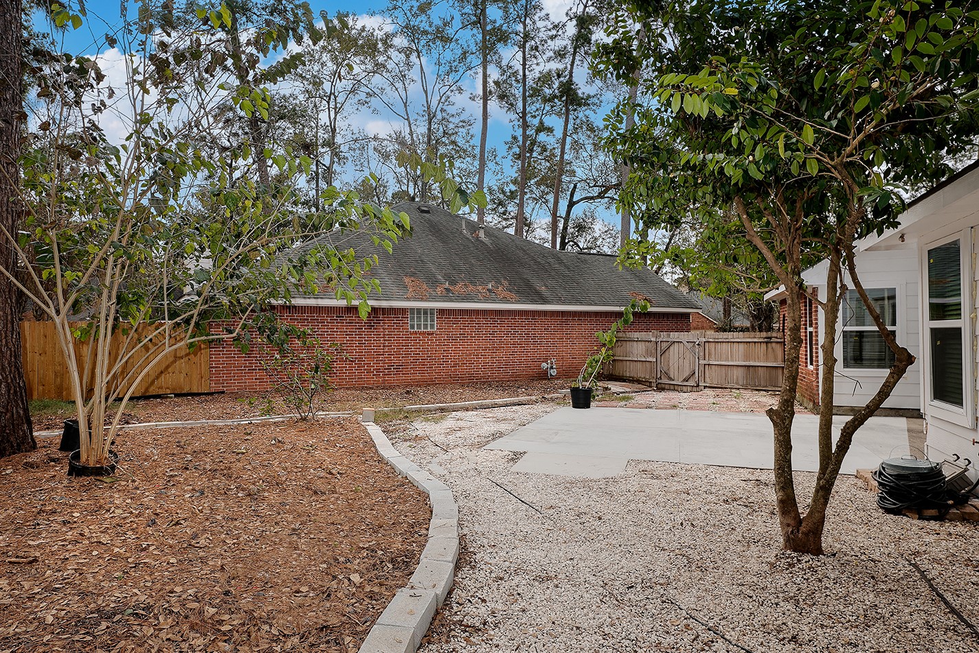 The spacious backyard has a mix of gravel and mulch landscaping, featuring mature trees and a patio area.