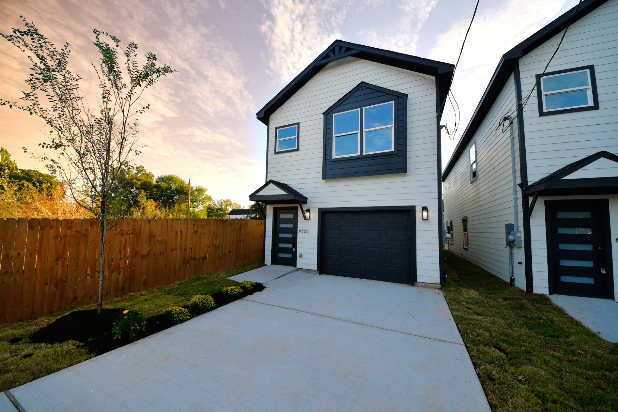 The home's modern farmhouse-inspired exterior combines cement board siding, stone accents, dark trim, and a welcoming covered entry. A private driveway leads to the attached 1-car garage.