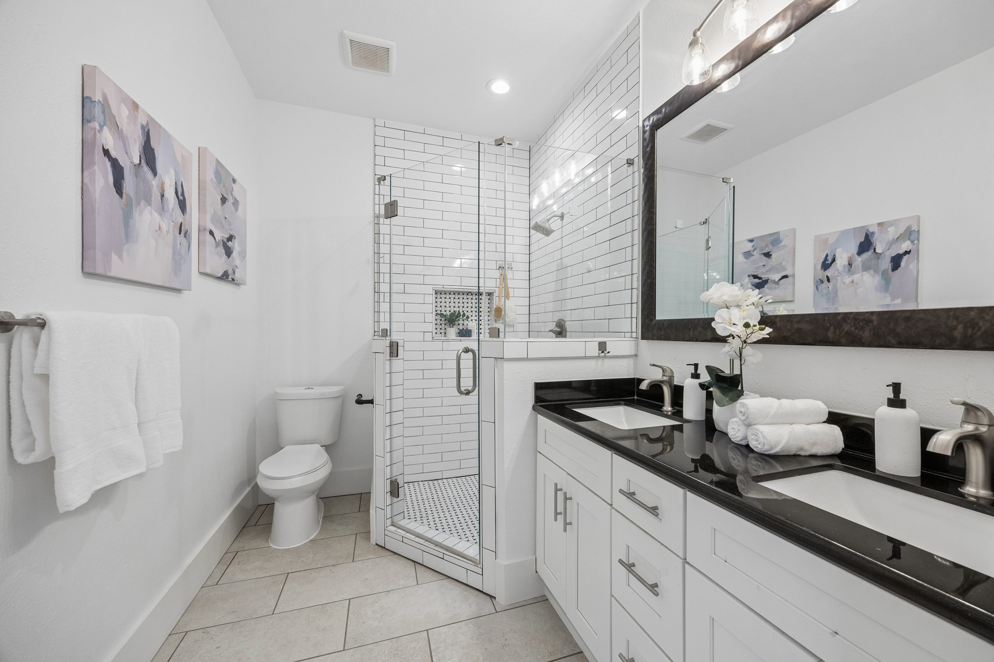Sleek and modern bathroom featuring a glass-enclosed shower with subway tile, dual-sink vanity with black countertops and elegant fixtures.