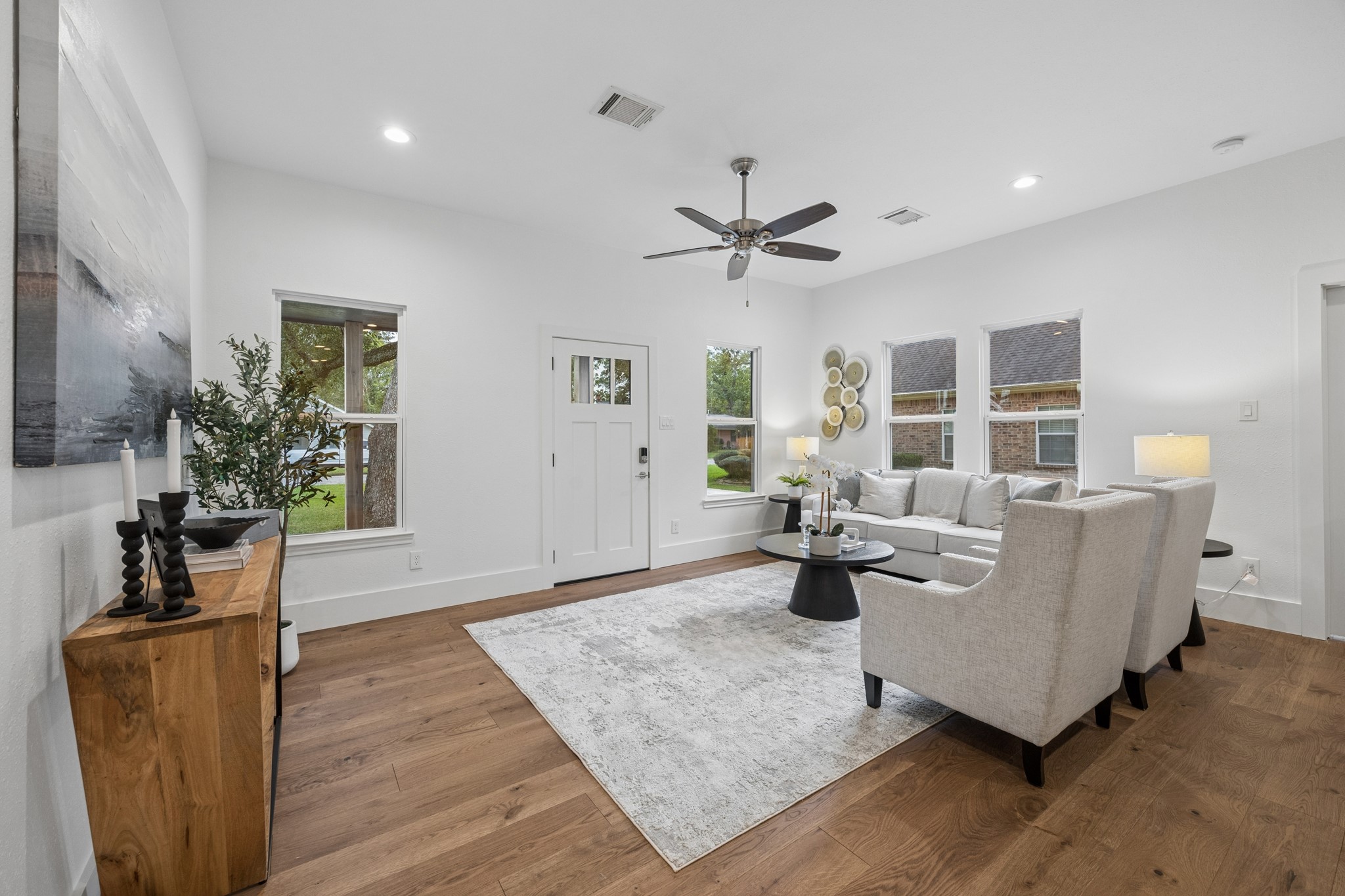 Bright and inviting living room featuring a stylish ceiling fan, elegant wood flooring, and ample natural light from multiple windows.