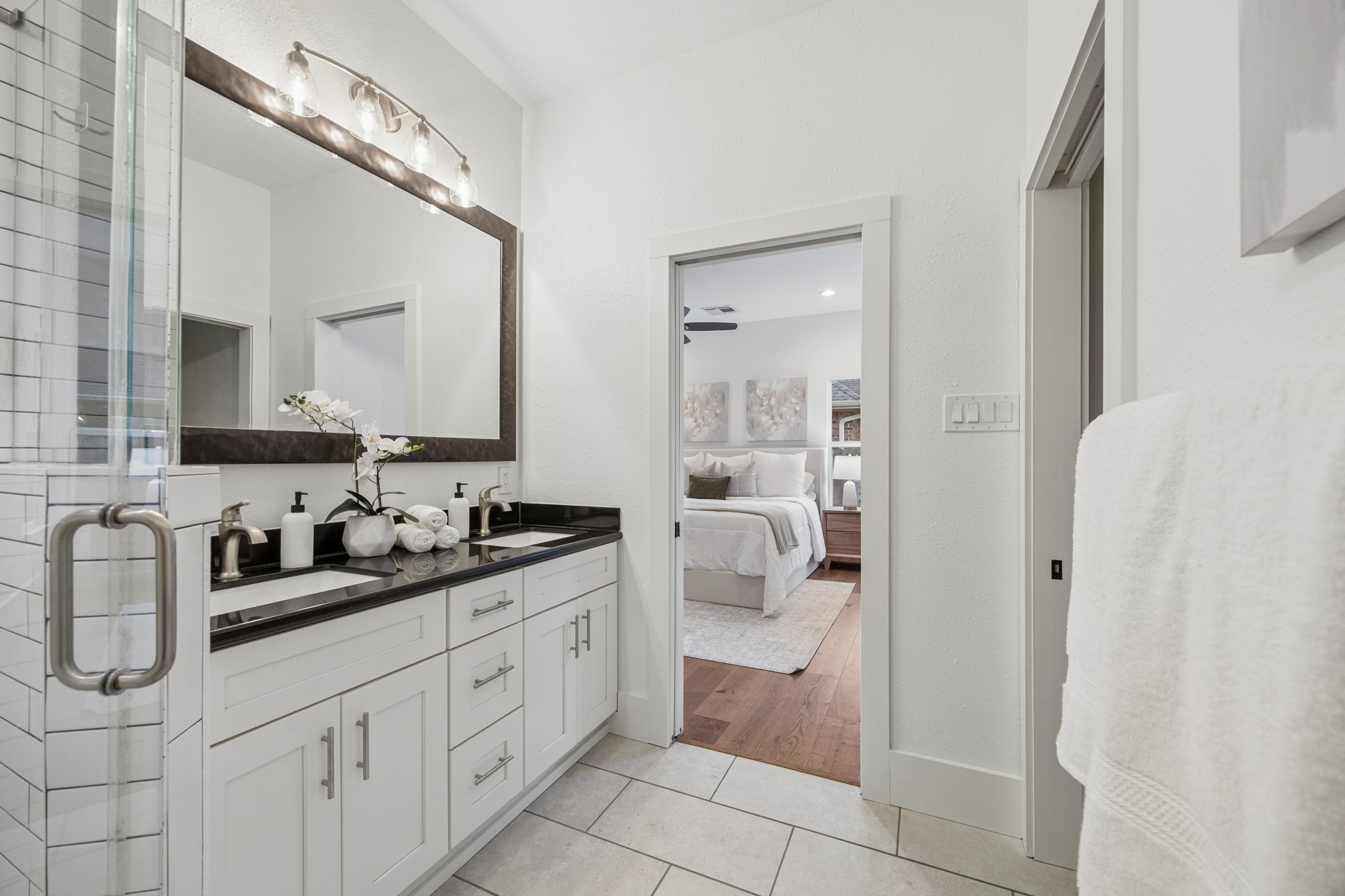 Primary bathroom features a double vanity with sleek black countertops, modern fixtures, and ample storage, seamlessly connected to a cozy bedroom.