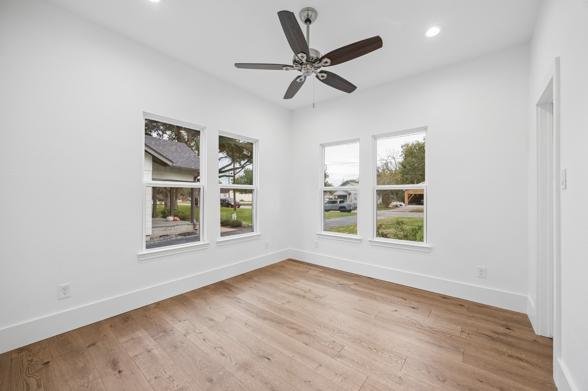 Bright and airy bedroom with large windows, wood flooring, and a stylish ceiling fan.