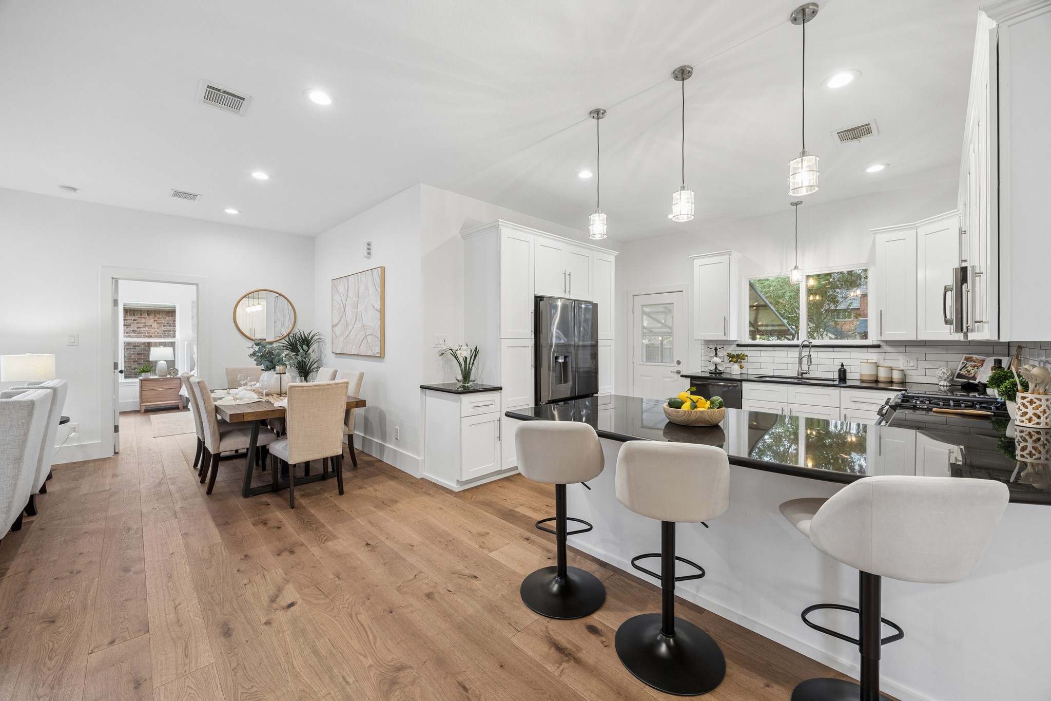 Spacious kitchen with sleek black countertops, elegant pendant lighting, and ample seating at the island. Adjoining dining area perfect for entertaining.