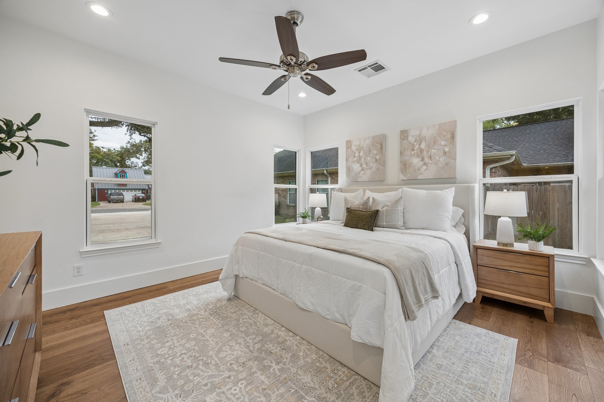 Primary bedroom featuring hardwood floors, large windows, and a ceiling fan.