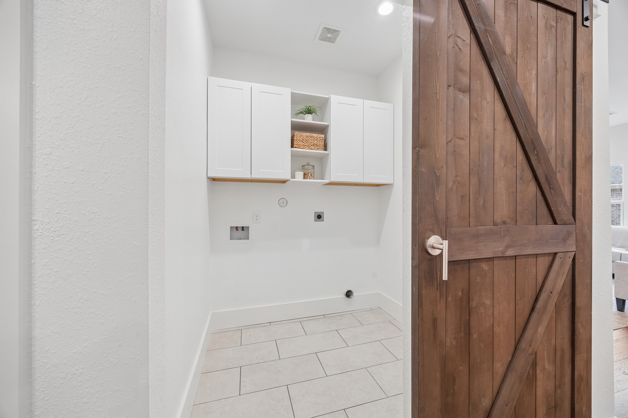 Convenient laundry room with sleek white cabinets and rustic wooden barn door, offering both style and functionality.
