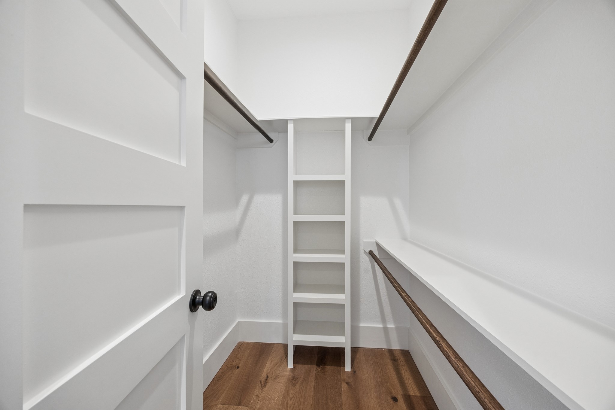 Spacious walk-in closet featuring elegant built-in shelving and rich wooden floors, offering ample storage space.