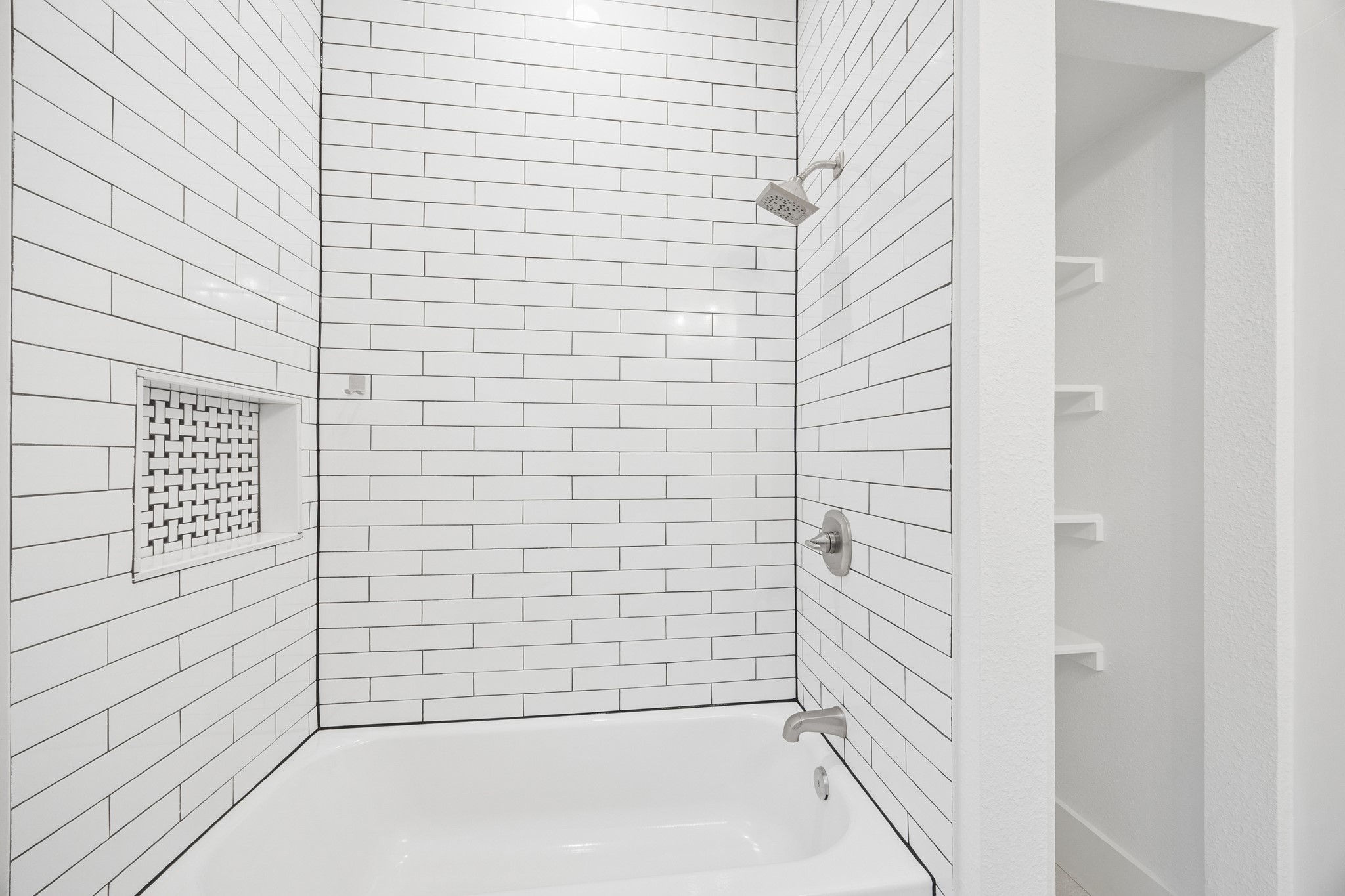 Sleek bathroom featuring a modern white subway tile design, spacious tub, and built-in shelving for convenient storage.