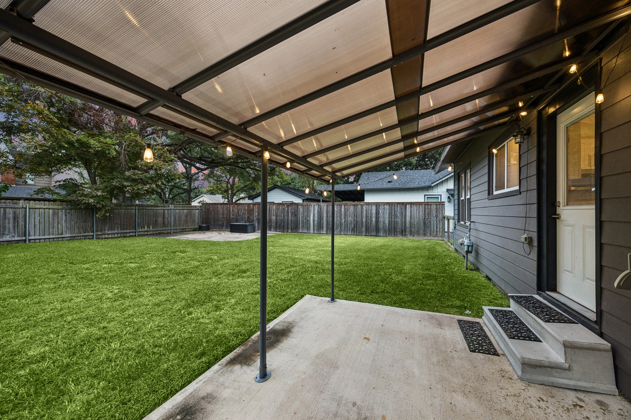 Charming backyard features a spacious covered patio with warm lighting, perfect for outdoor gatherings.