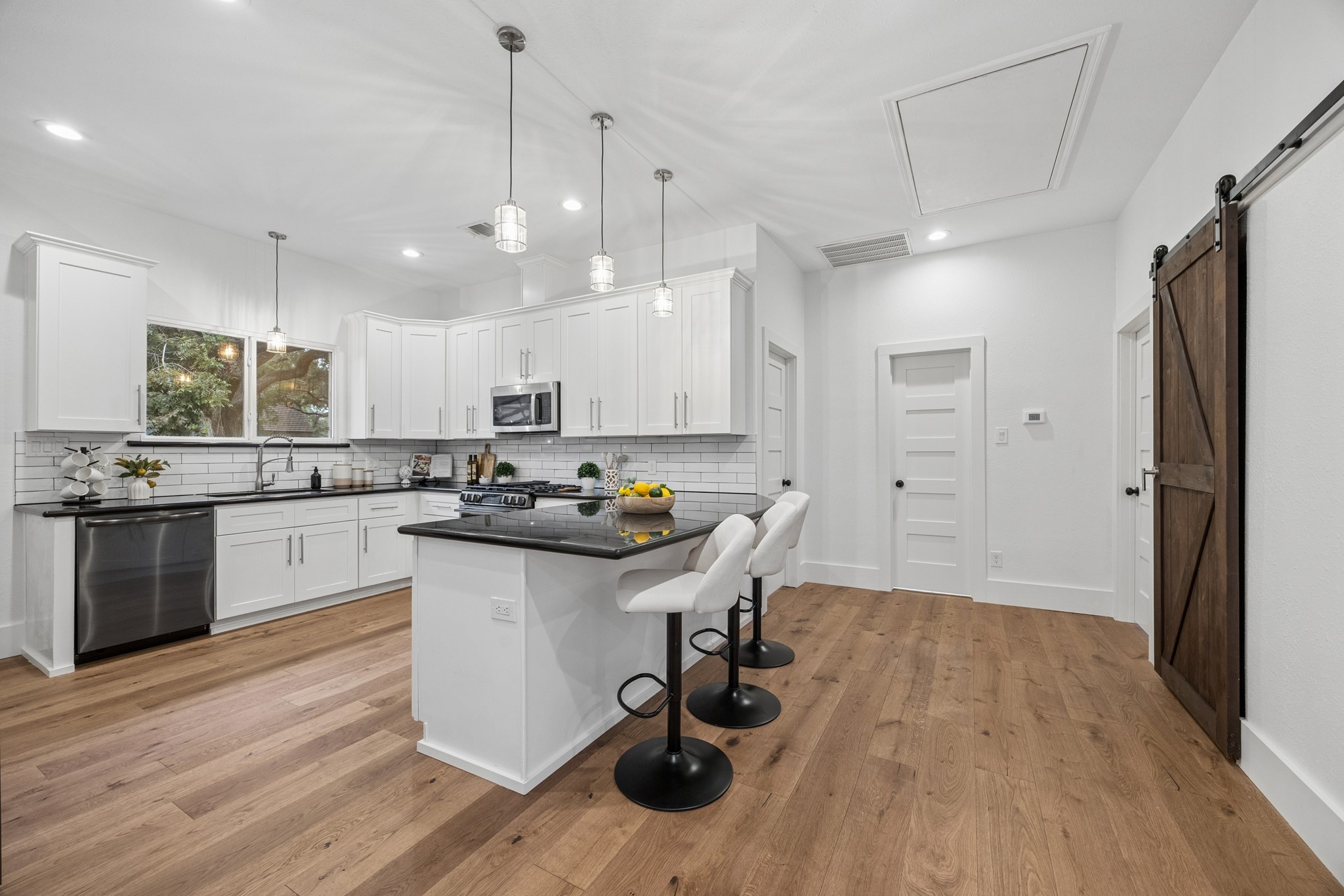 Modern kitchen with sleek white cabinetry, stainless steel appliances, and a stylish subway tile backsplash. Features an inviting island with seating and elegant pendant lighting.