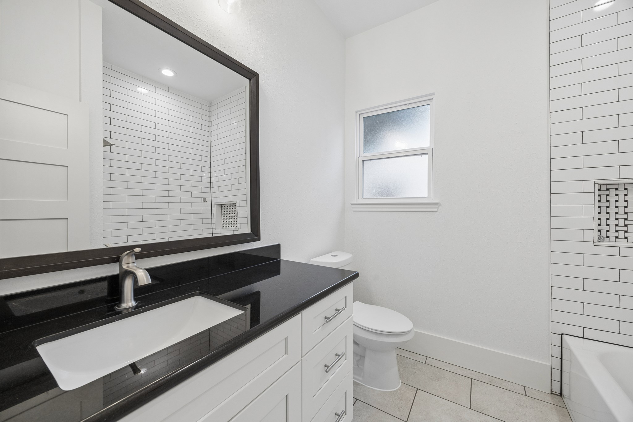 Sleek bathroom featuring a modern black countertop, stylish white cabinetry, and elegant subway tile accents.