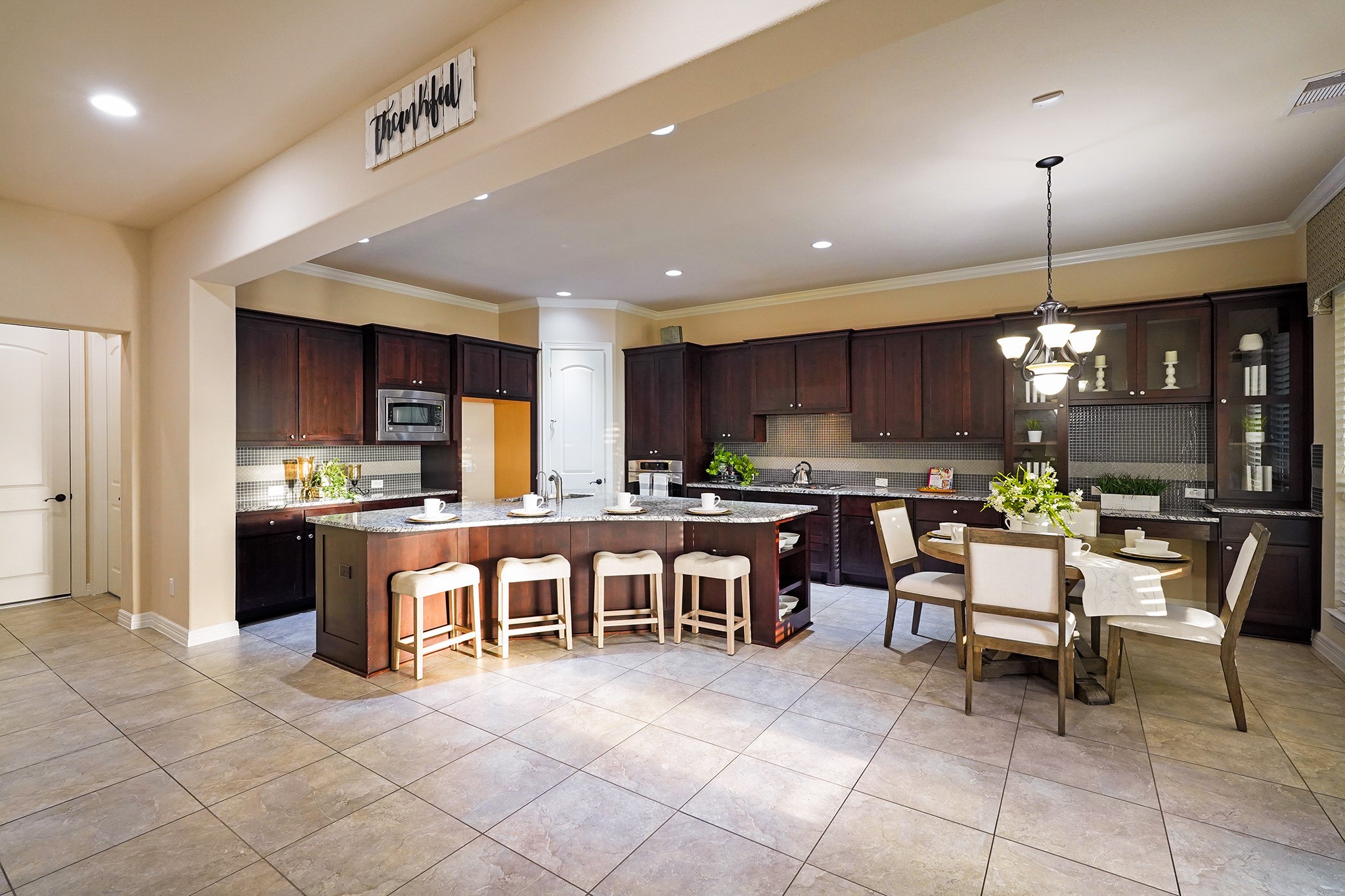 The kitchen features dark wood cabinetry, a large island with seating for four, and ample counter space. It's well-lit with recessed lighting and a stylish chandelier over the adjacent dining area, creating a welcoming atmosphere for cooking and entertaining.