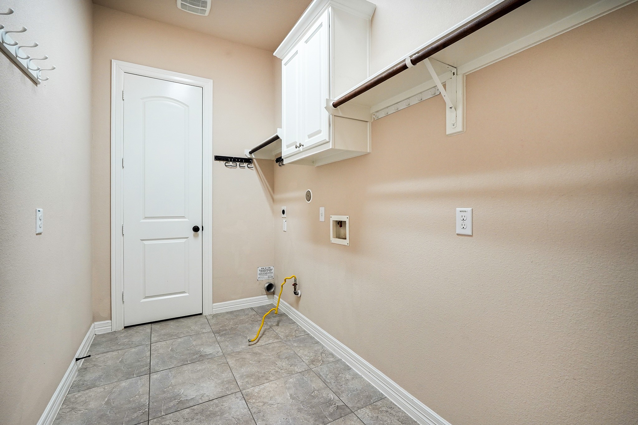 This oversized laundry room with tiled flooring, a white door, wall-mounted cabinets, and connections for a washer and dryer features ample shelving for storage.